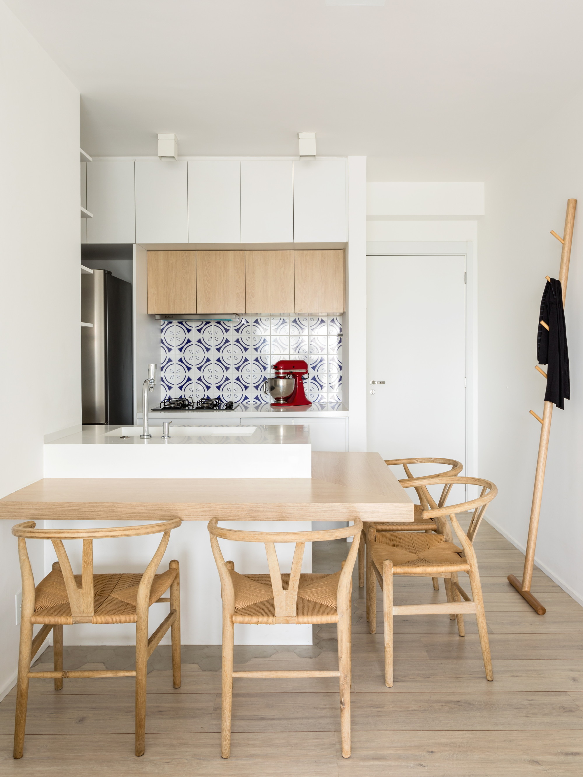 Kitchen peninsula with oak counter, blue patterned tile backsplash and wishbone chairs, a black coat hanging on a leaning wooden rack