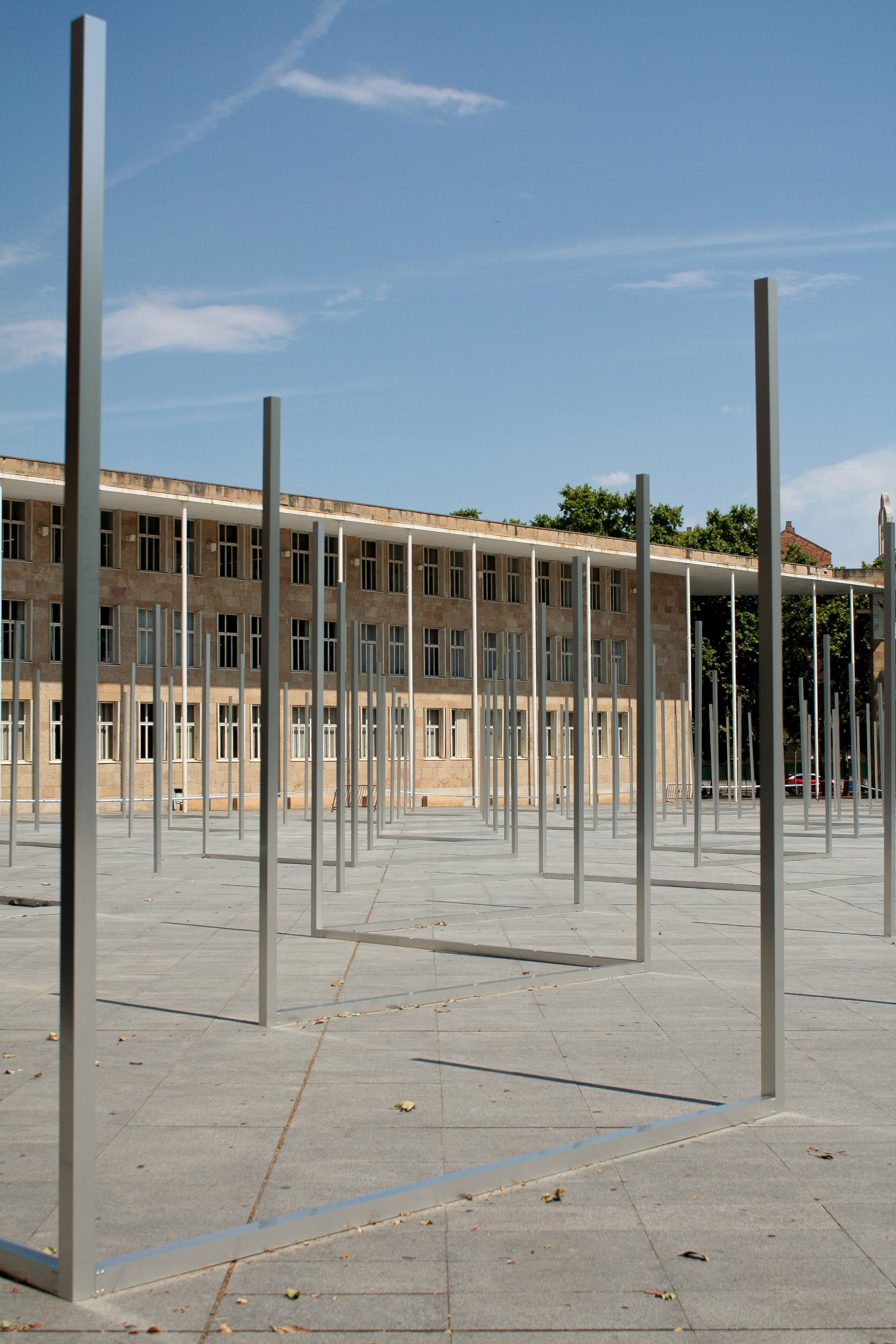 Low-angle view of a steel frame and its floor rail on grey paving, with a long building behind under a blue sky