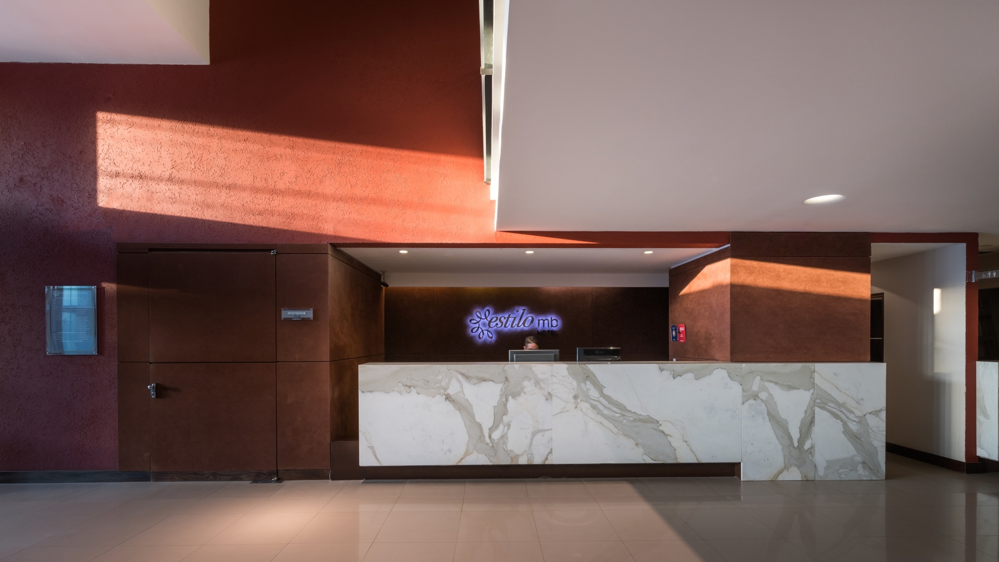 Marble-fronted reception desk in front of a textured red wall crossed by a diagonal band of afternoon sunlight