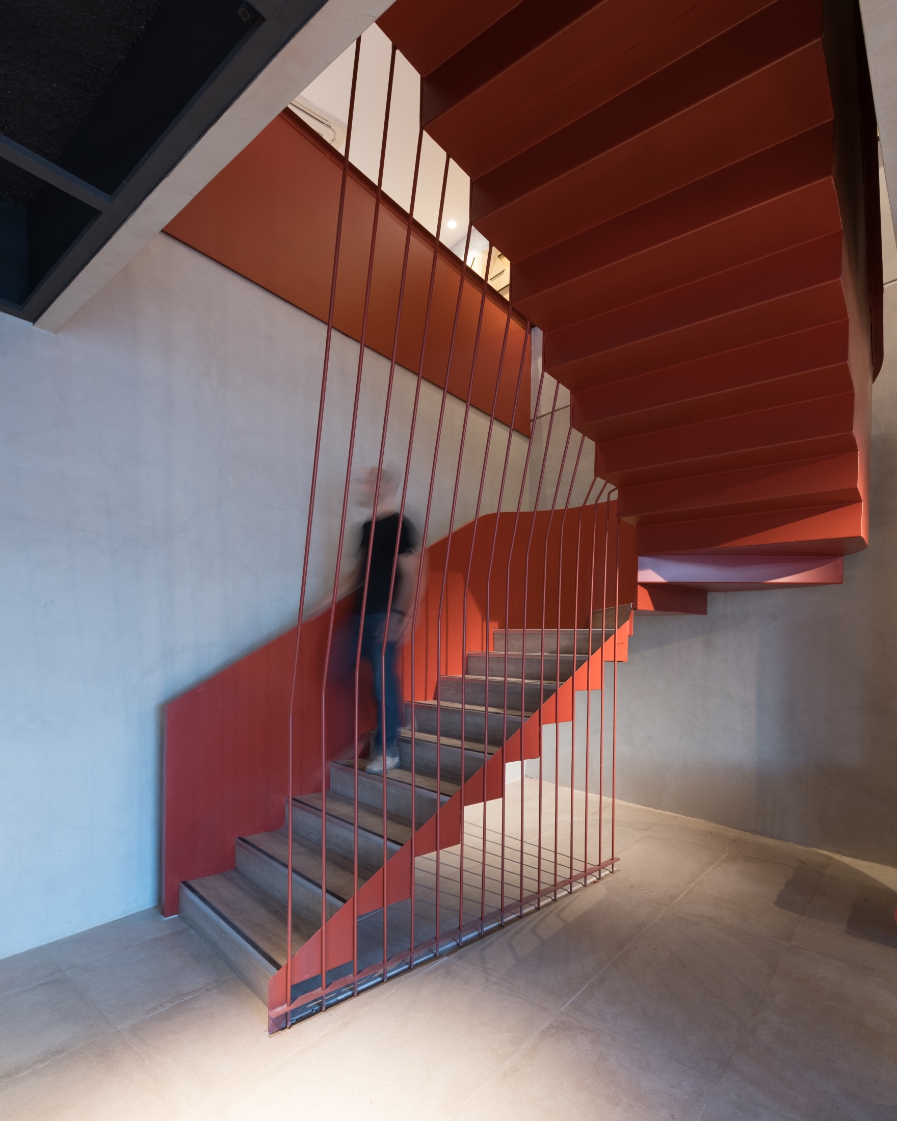 Folded red steel staircase with thin vertical rods, a blurred person climbing past a concrete wall
