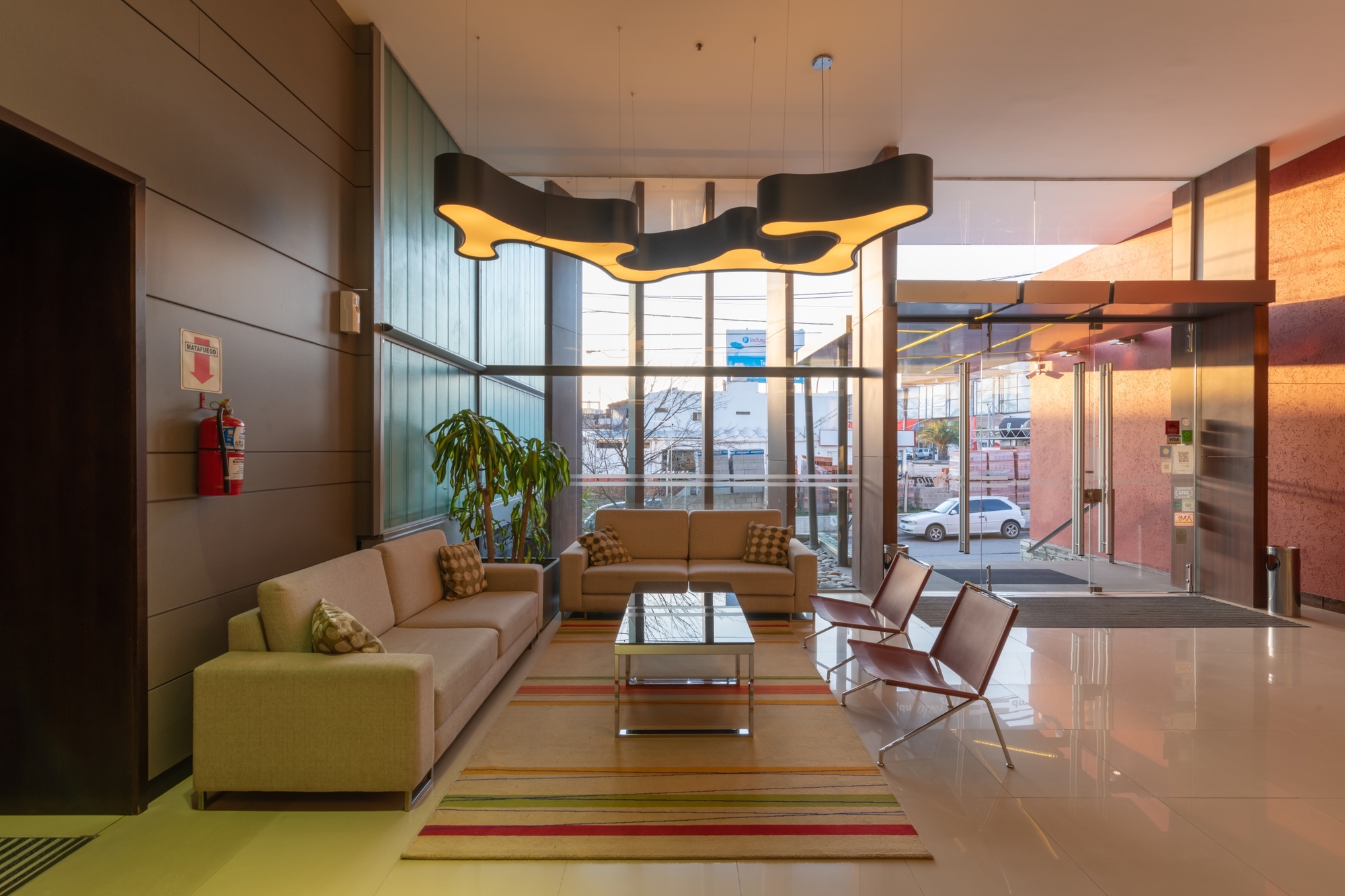 Lobby seating area with beige sofas, a striped rug and a wavy pendant lamp beside the glass entrance