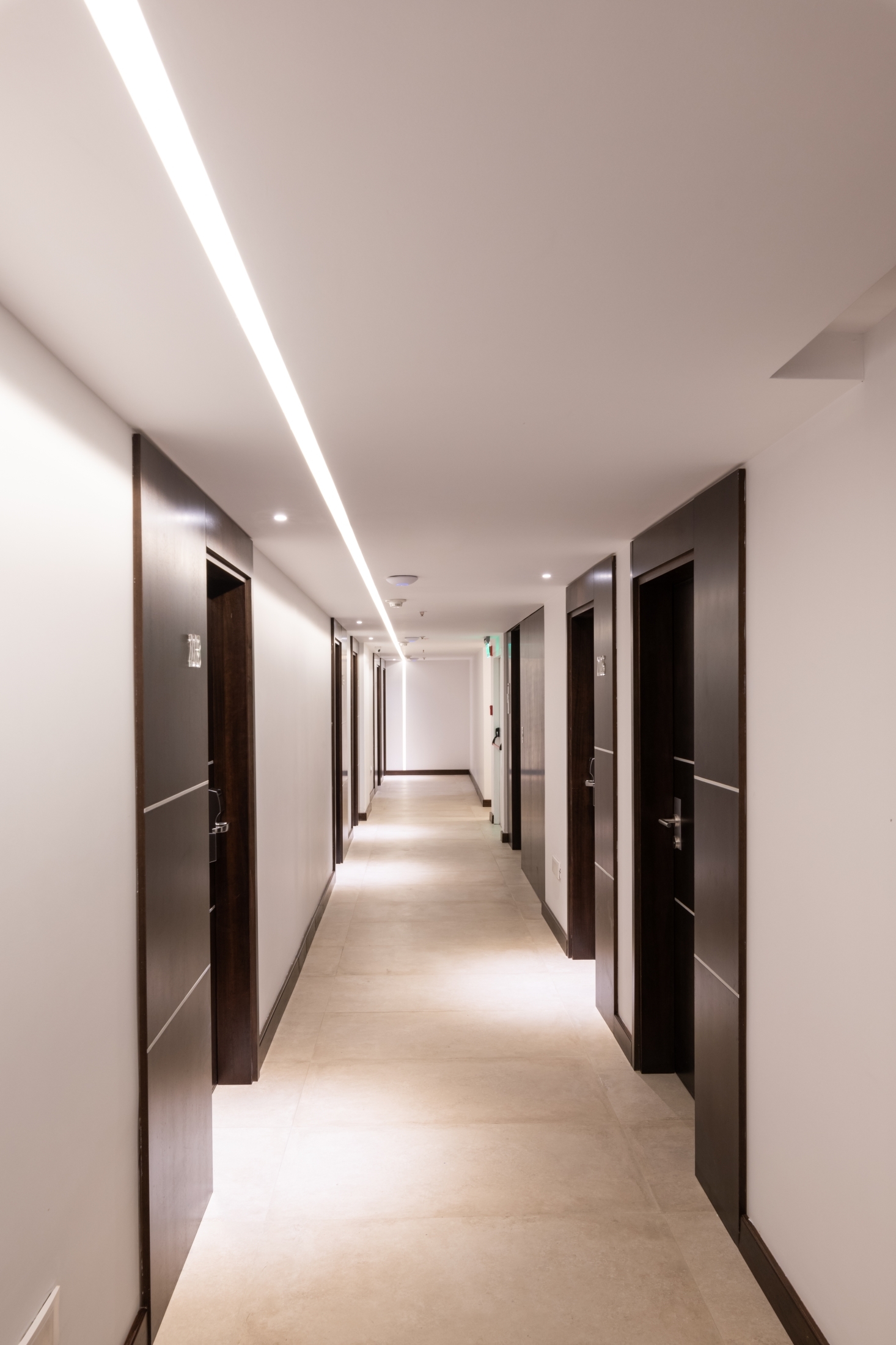 Hotel corridor with dark wood door frames and a linear ceiling light running down its length