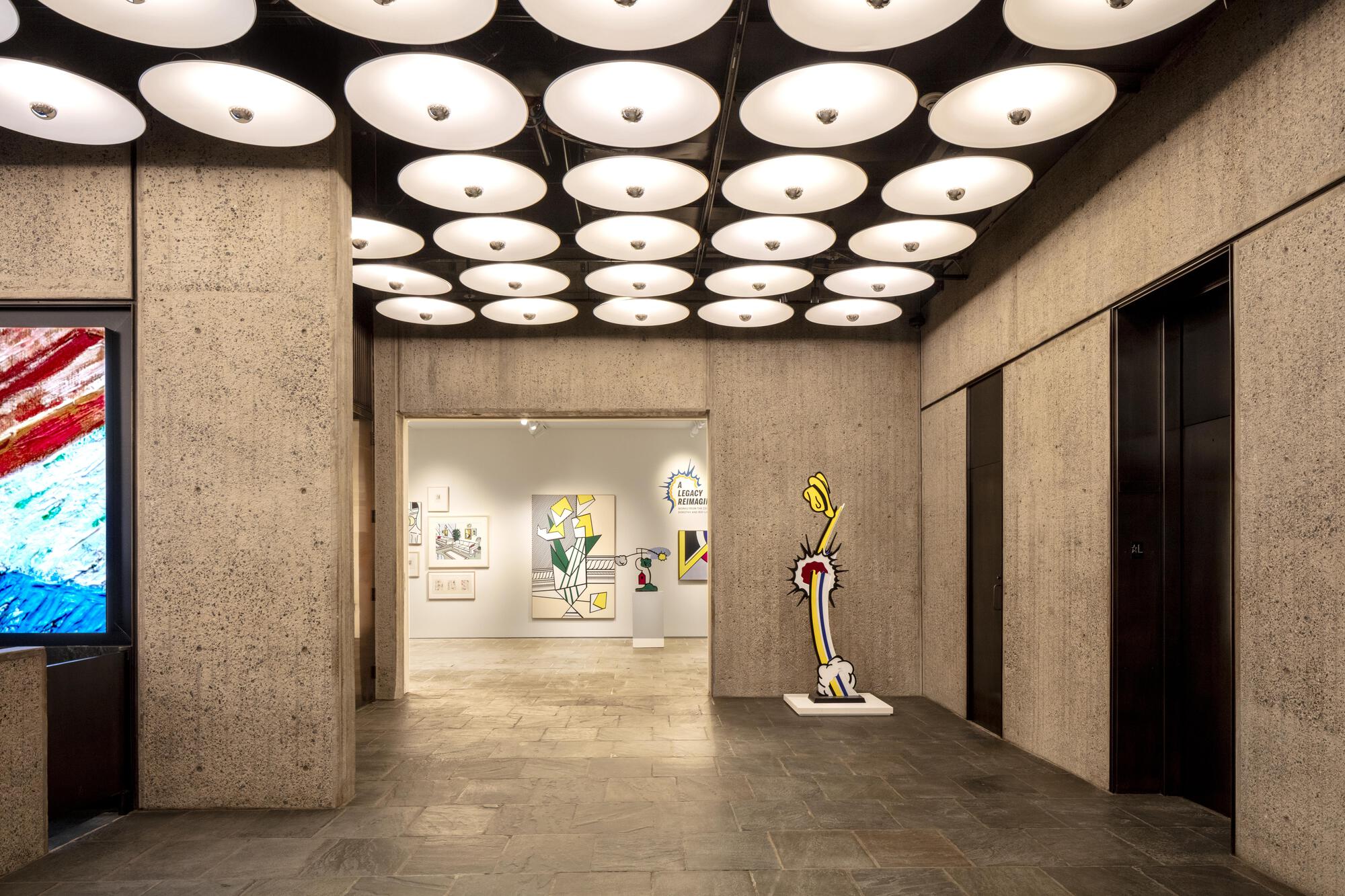 Lobby with board-formed concrete walls, a grid of round white ceiling lights and a pop art sculpture on a slate floor