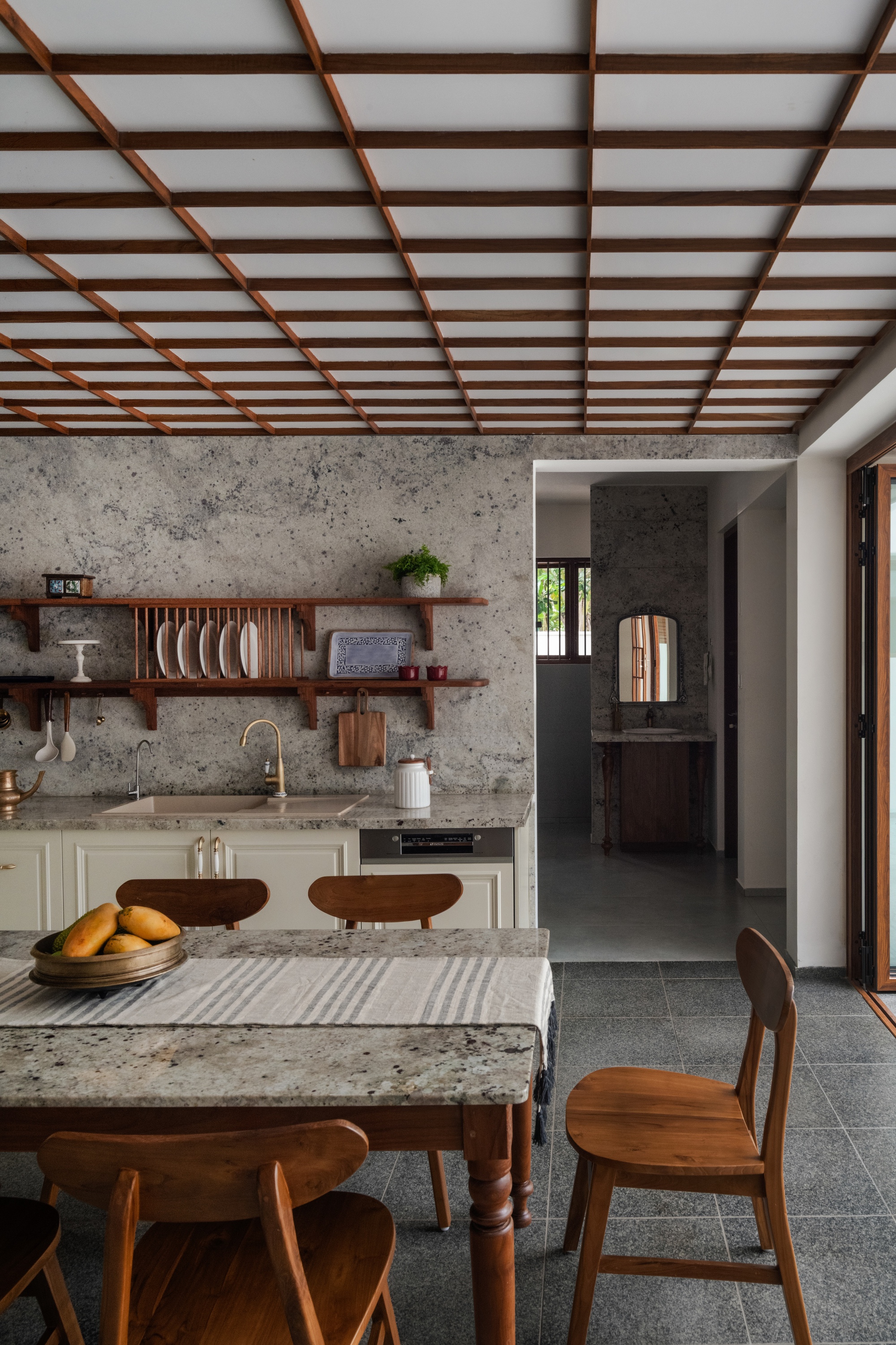 Kitchen with granite topped table, open timber shelves and a lattice ceiling, with a bowl of mangoes in daylight
