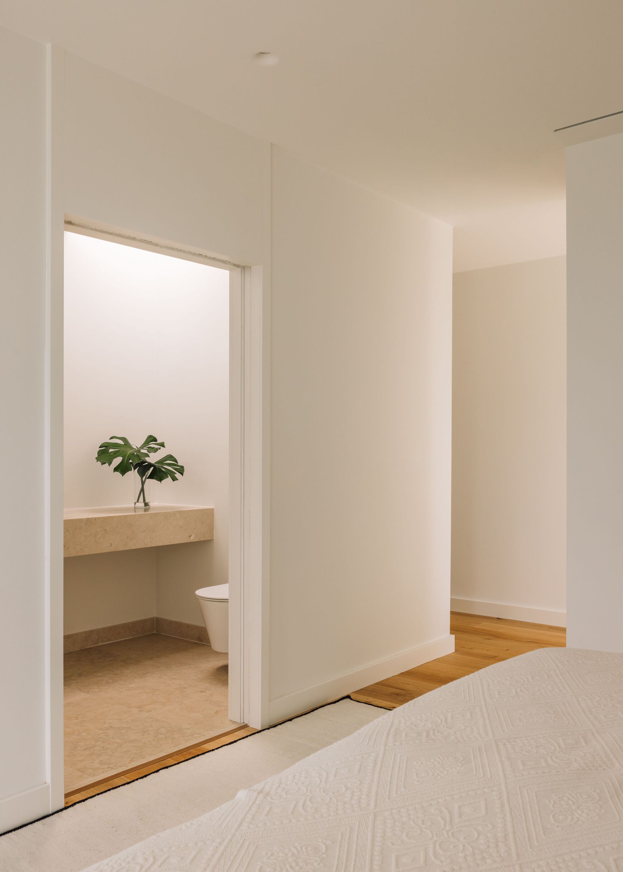 View from the bedroom into a small stone-floored toilet room with a monstera leaf on a floating counter