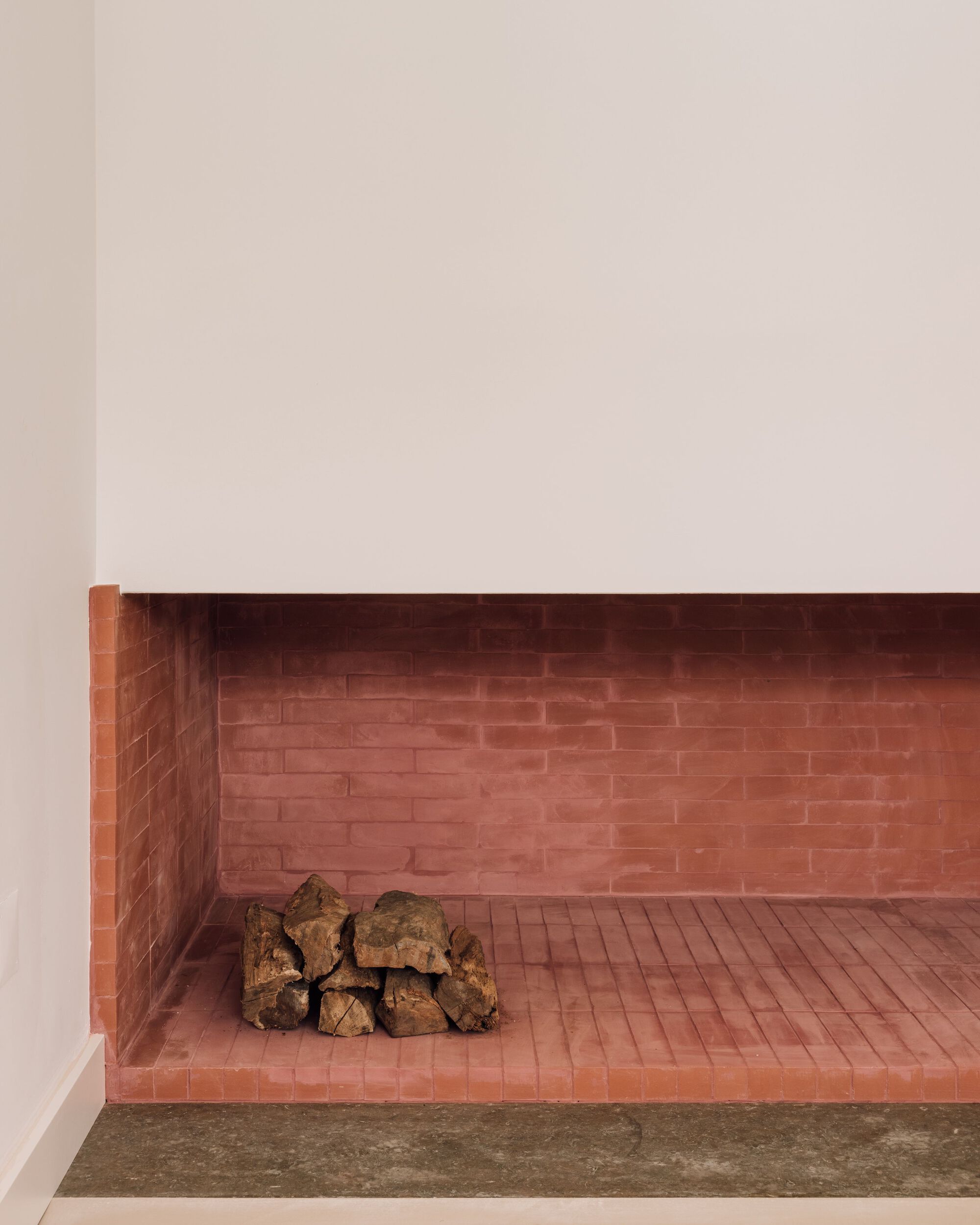 Close-up of a recessed fireplace built from terracotta-red brick, with a small stack of logs on the hearth