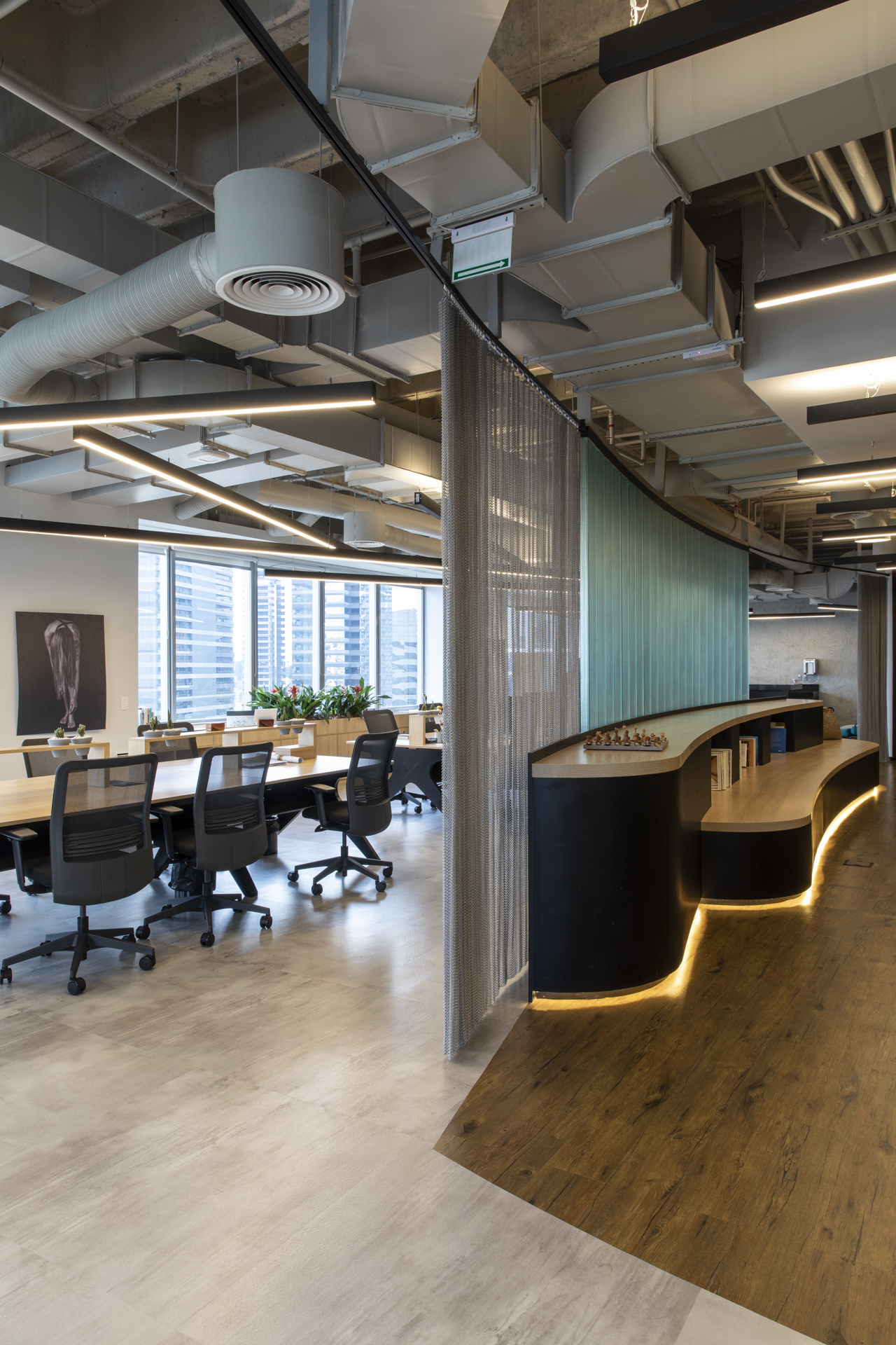 Vertical view of a curved bench with warm underlit base, mesh curtain and a green panel wall beside the desk area