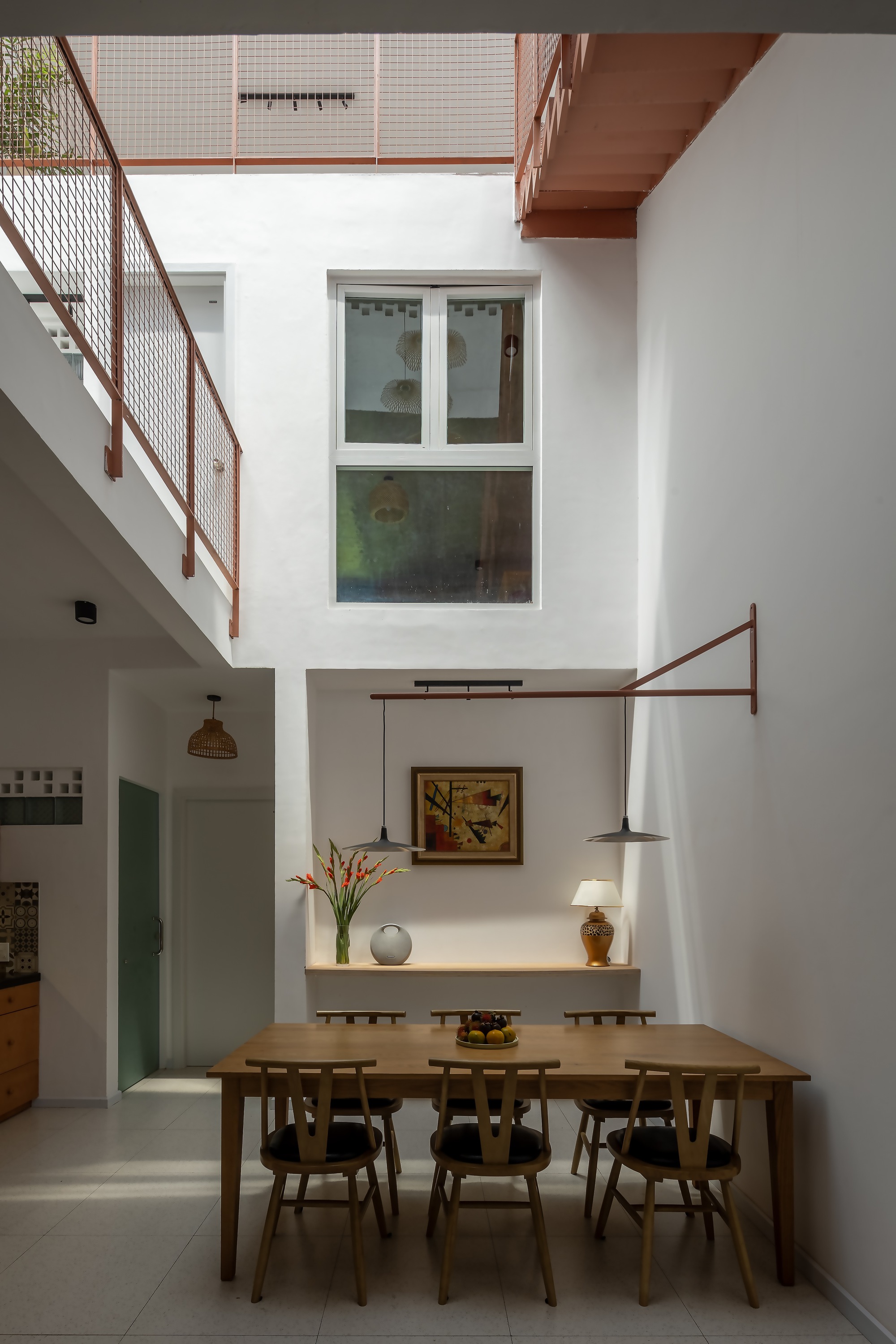 Double-height dining area with timber table and chairs, pendant lamps on a rust-colored arm, and a tall window above