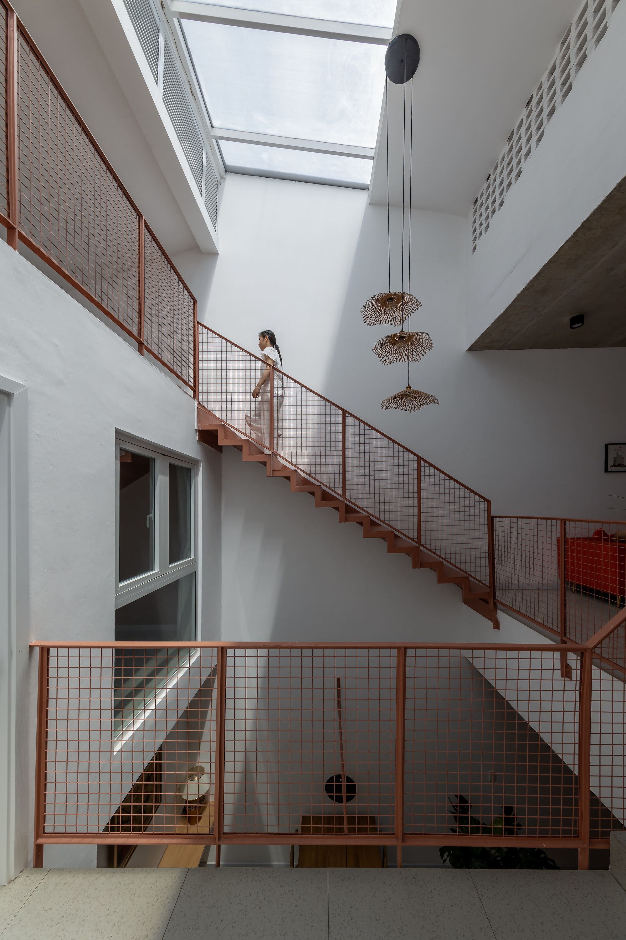Woman climbing a steel stair with mesh guardrails beneath a skylight, wicker pendant lamps hanging in the stairwell