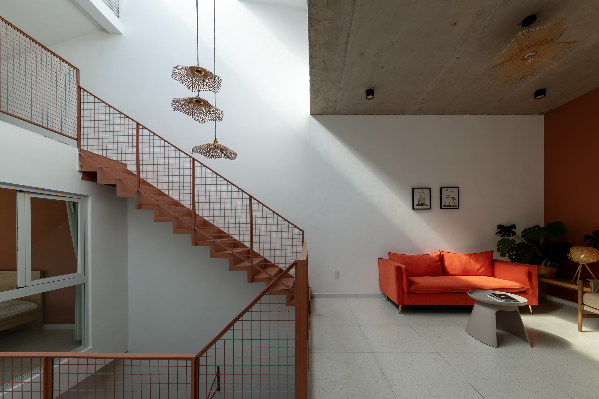 Terracotta steel staircase with mesh railings beside an orange sofa, with a shaft of daylight crossing the white wall