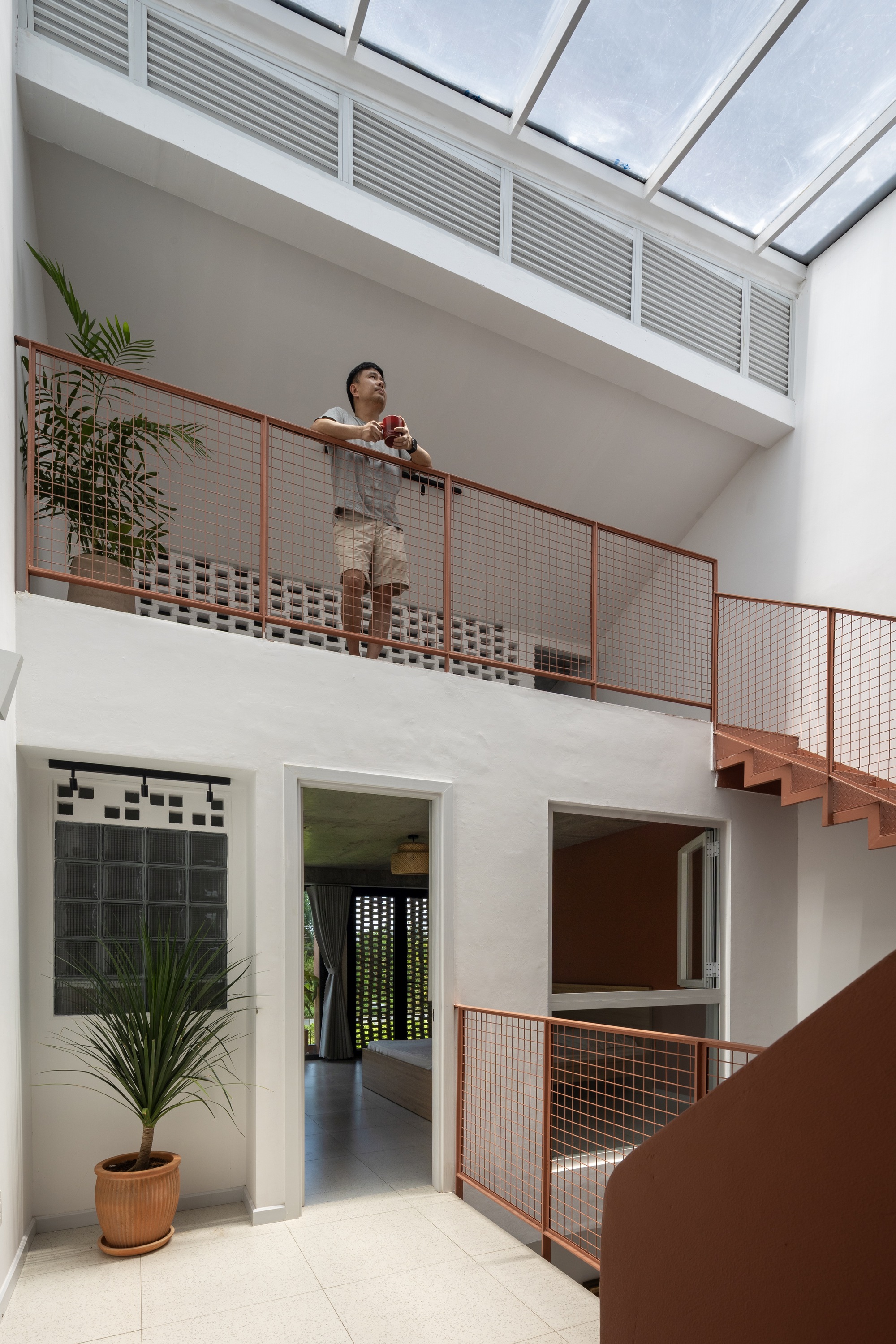 Double-height stairwell with a man leaning on the mesh balustrade beneath a louvred skylight and perforated block screen