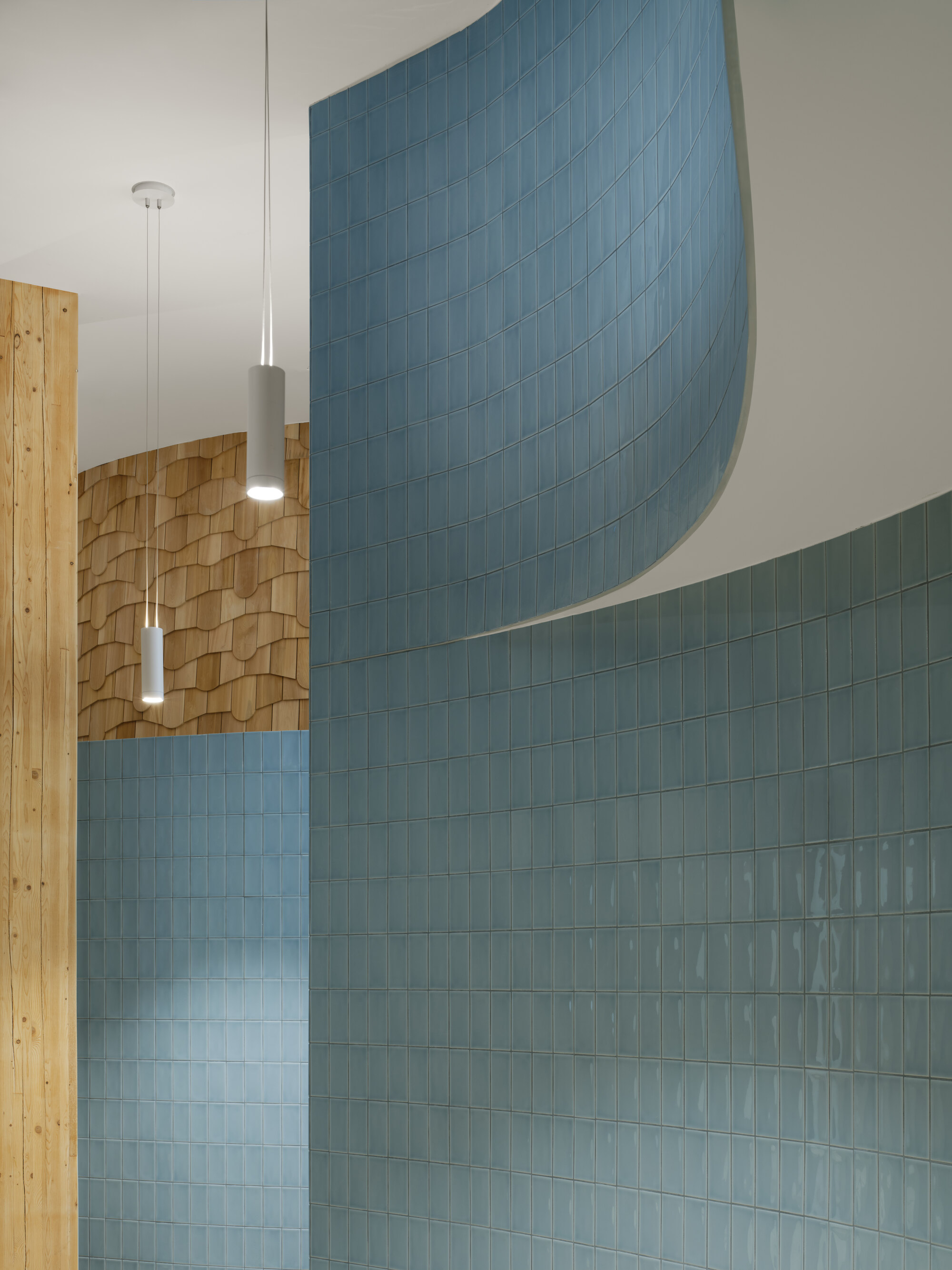 Curved blue glazed tile walls beside a timber post and wood shingle surface, lit by two white pendant lamps