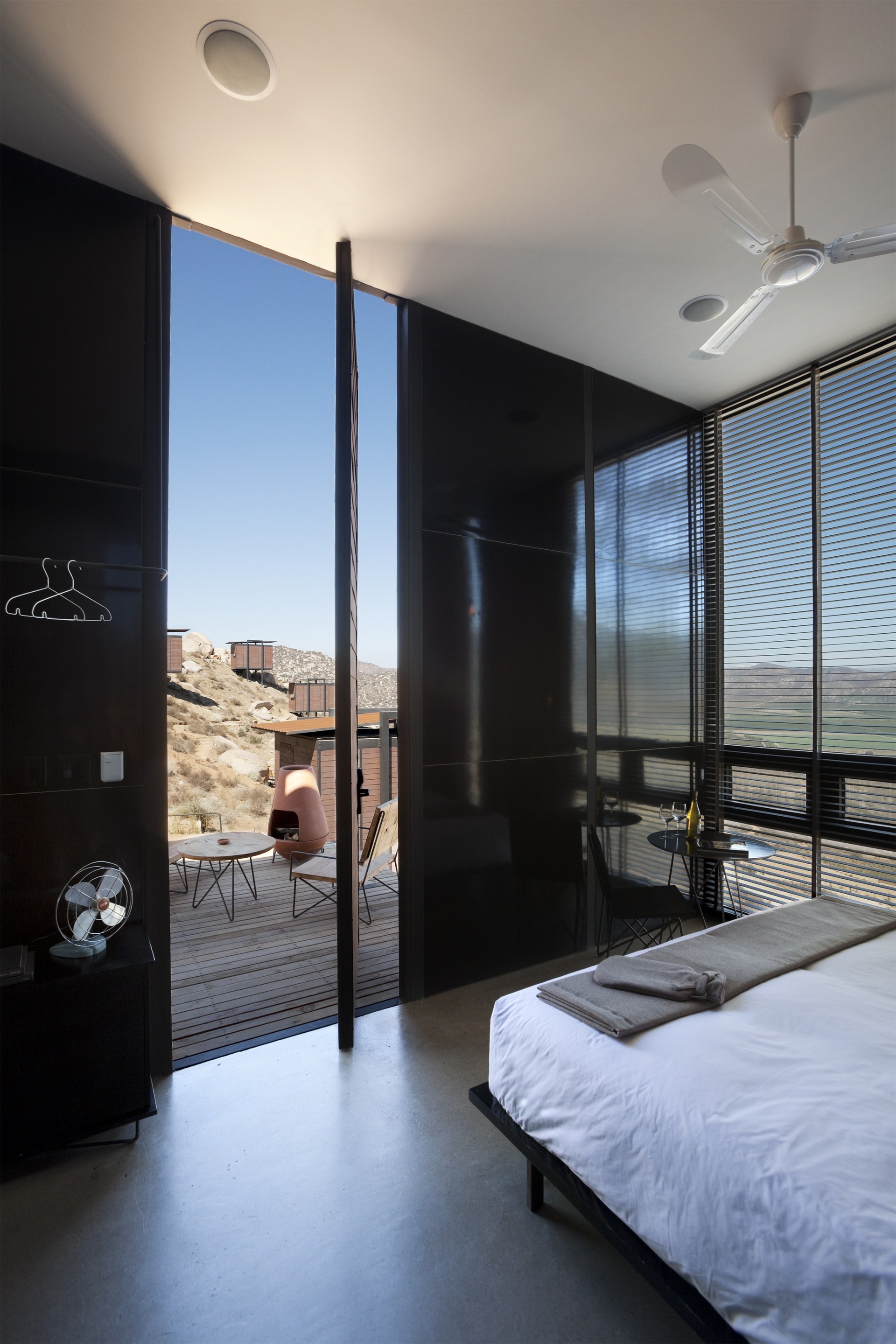 Bedroom looking through an open pivot door to the deck, with a ceiling fan and slatted blinds in daylight