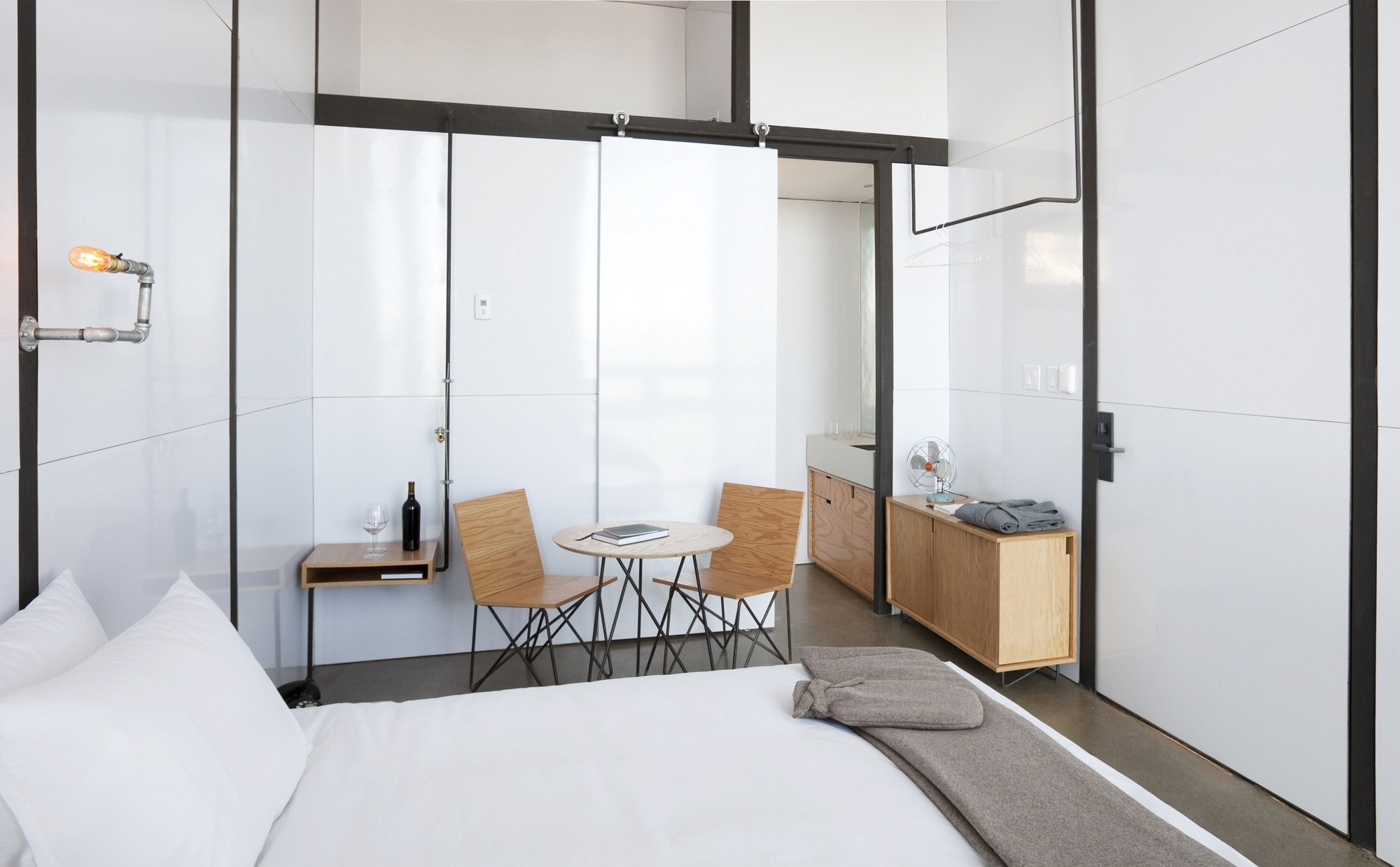Guest room with white glass panels, steel frames, plywood chairs and a sliding door leading to the bathroom in daylight