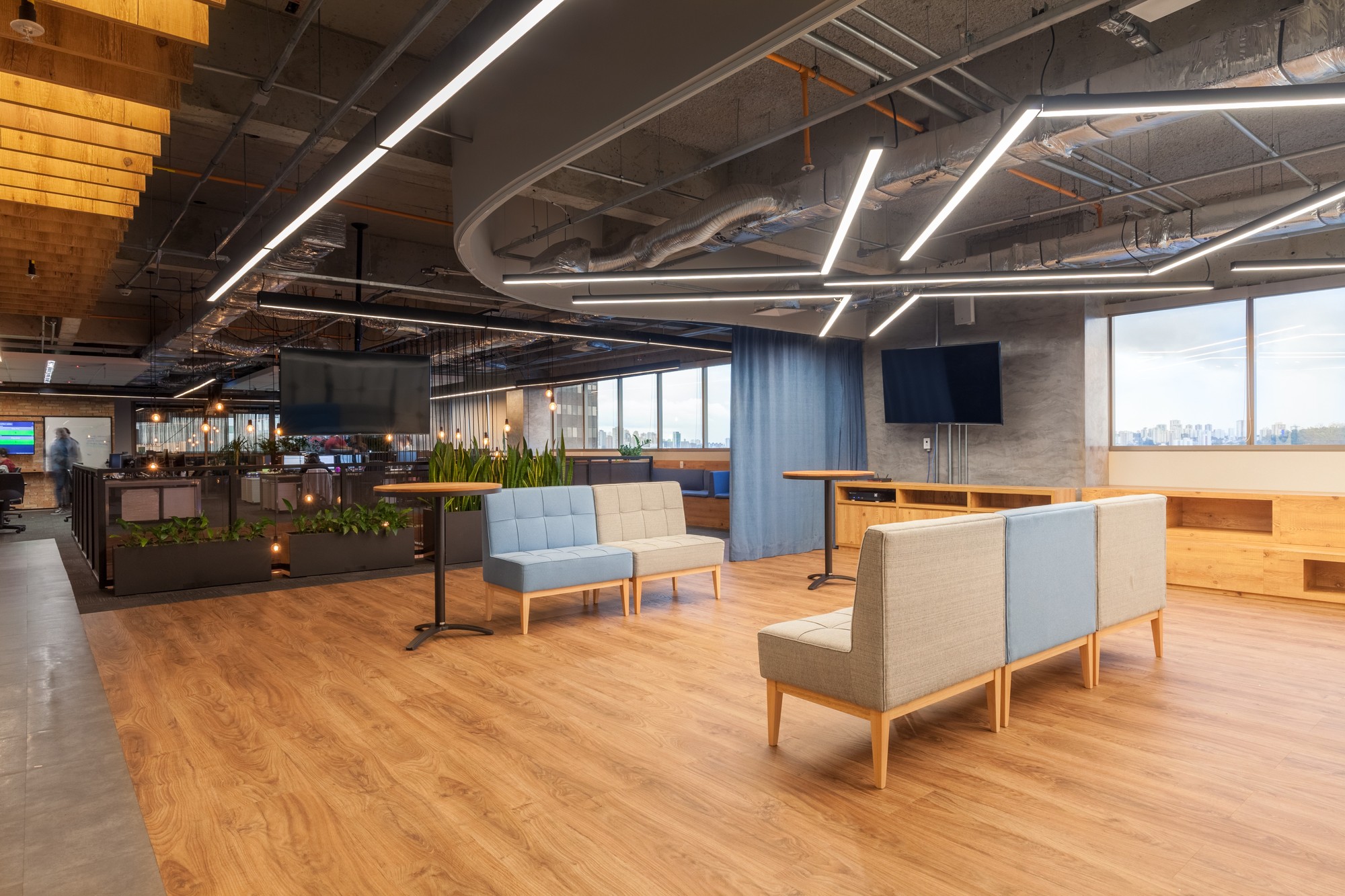 Lounge of pale blue and grey modular seats on a wood floor, with a blue curtain and city view through windows