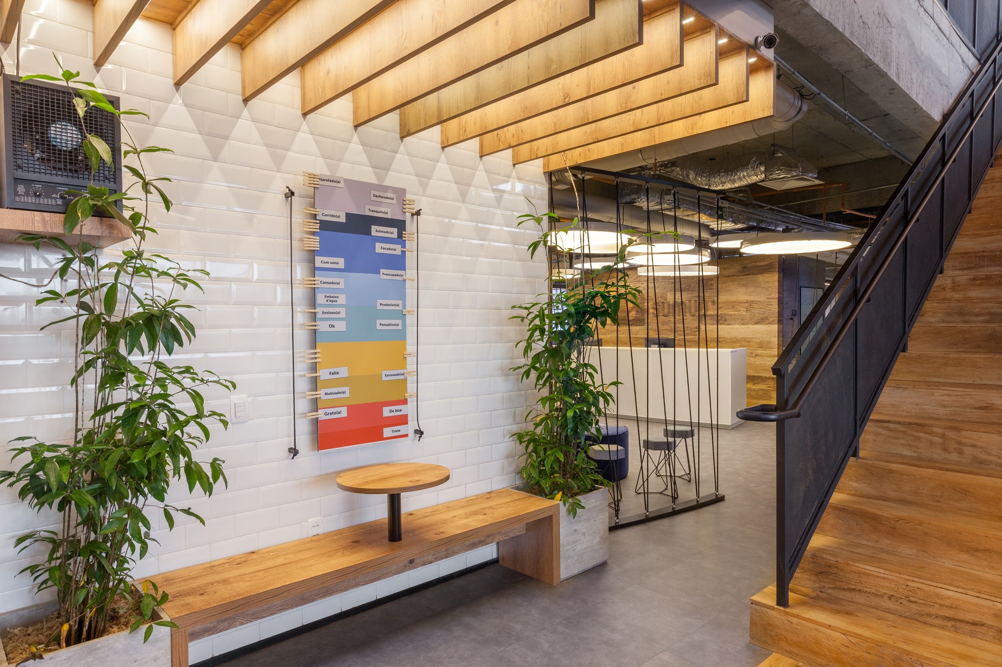 White tile wall with a colored wall chart above a timber bench, beside a wood-tread staircase with a black steel balustrade