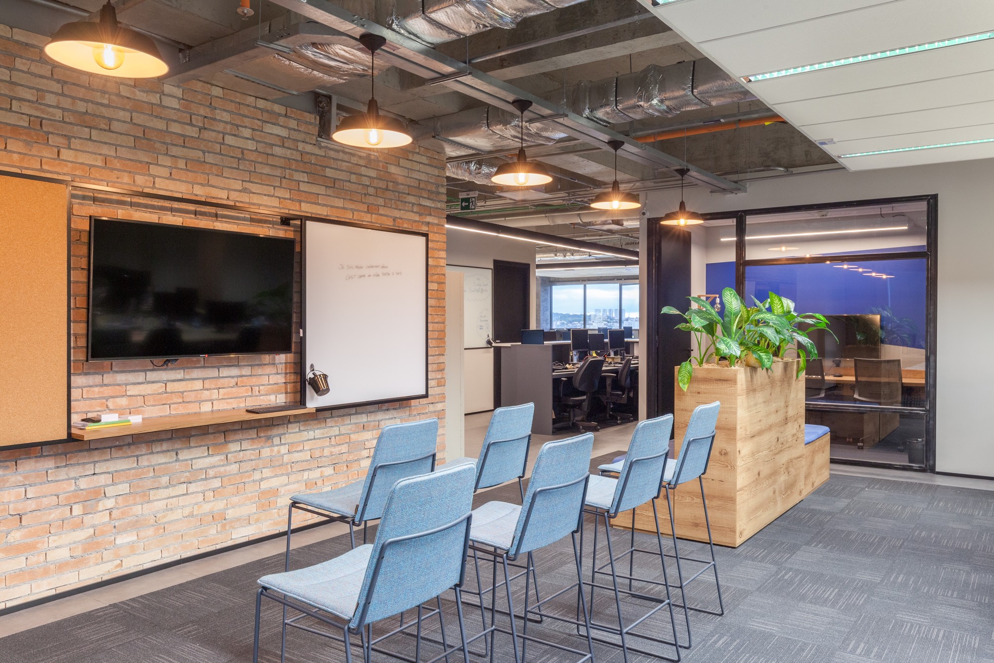 Exposed brick wall with a mounted screen and whiteboard, facing blue stools and a timber planter box holding green leaves