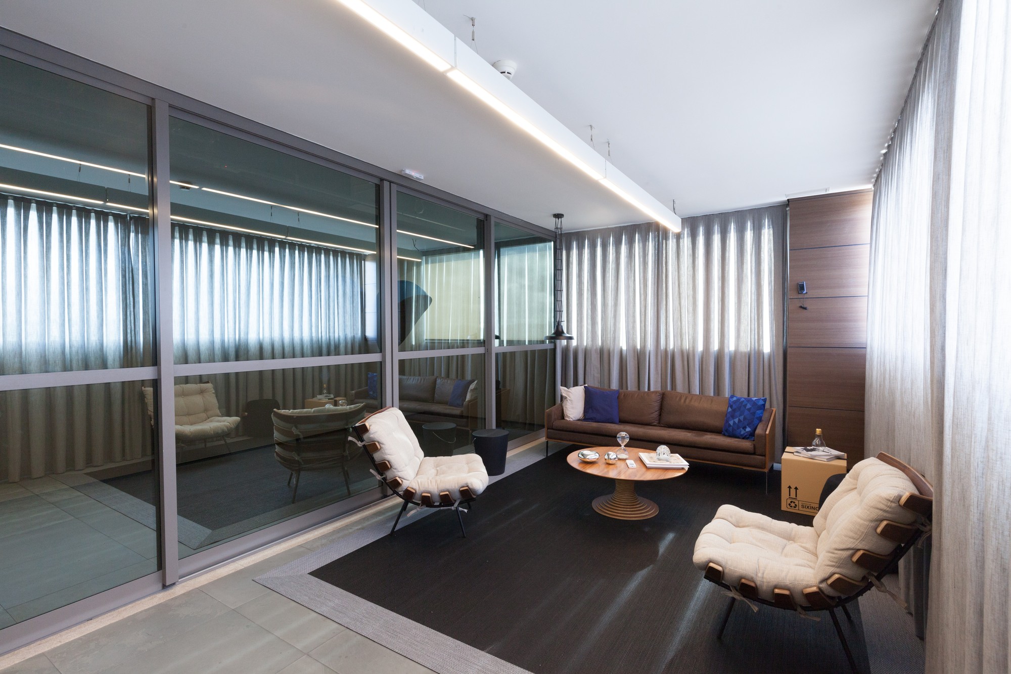 Lounge behind a glass partition with leather sofa, cushioned armchairs and round timber coffee table, sheer curtains filtering daylight
