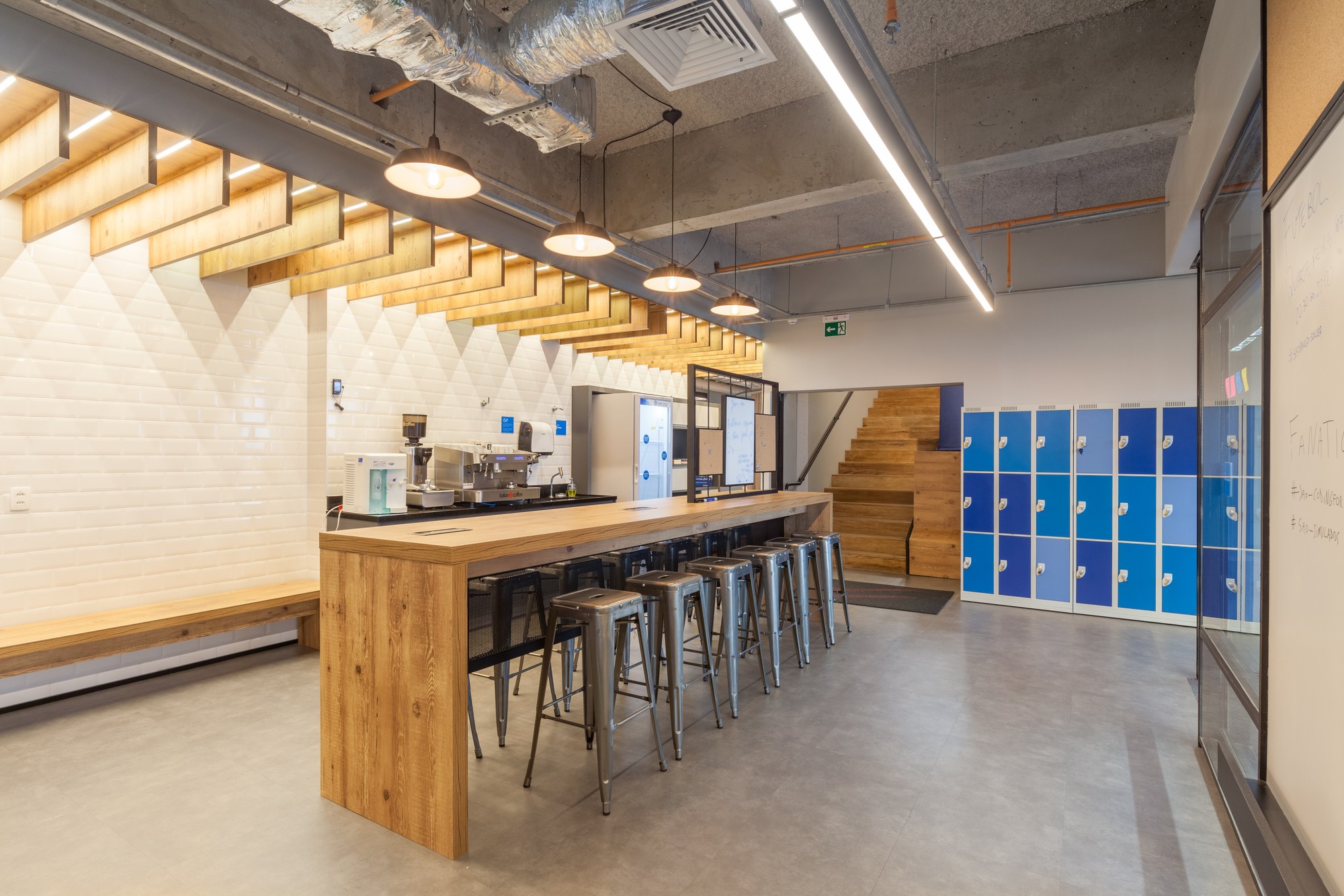 Pantry with a long timber counter, metal stools, white tile wall, blue lockers and a stepped timber seating stair behind