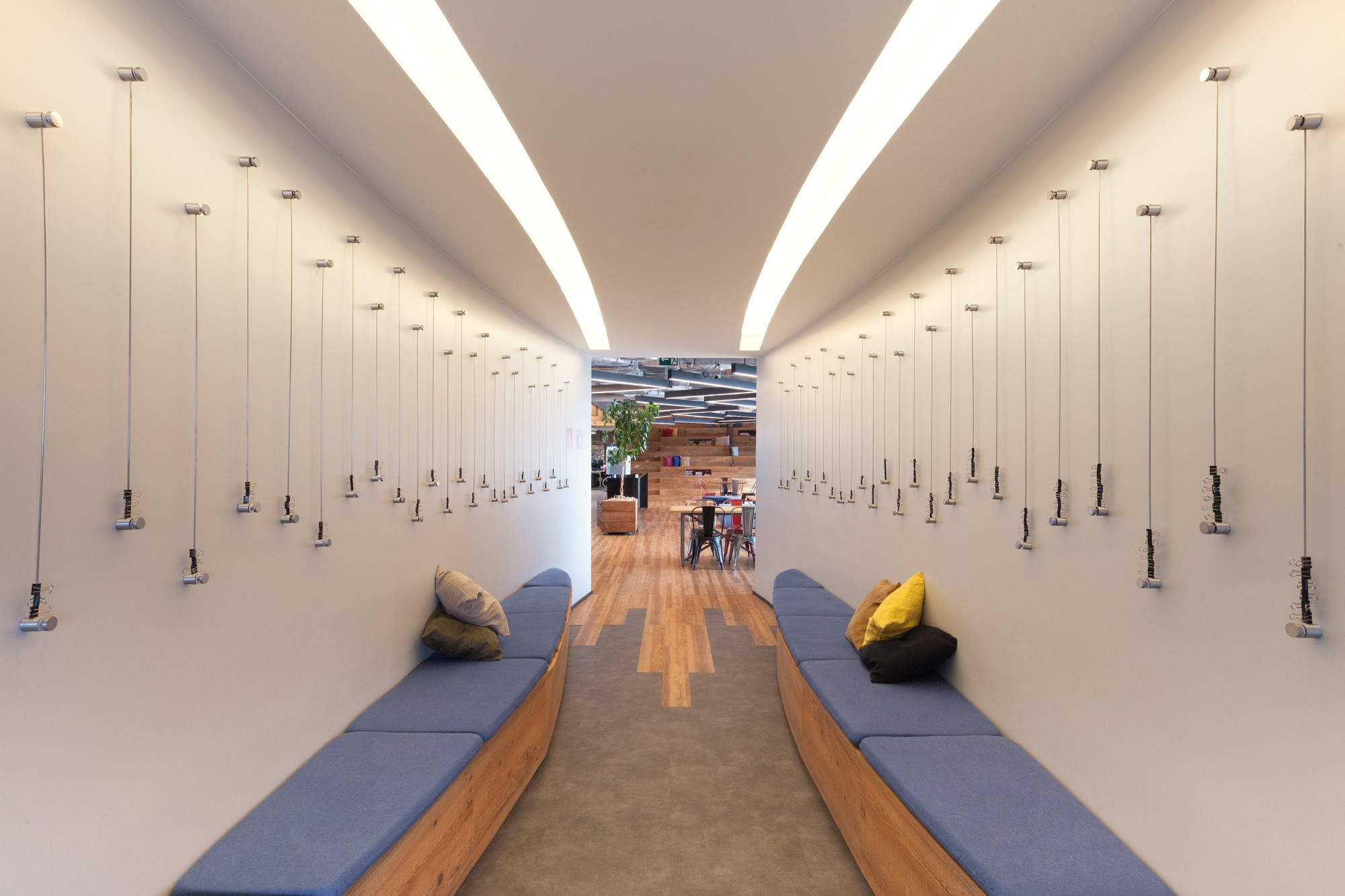 Narrow corridor lined with blue-cushioned timber benches and rows of hanging cable pulls, with soft light from curved ceiling coves