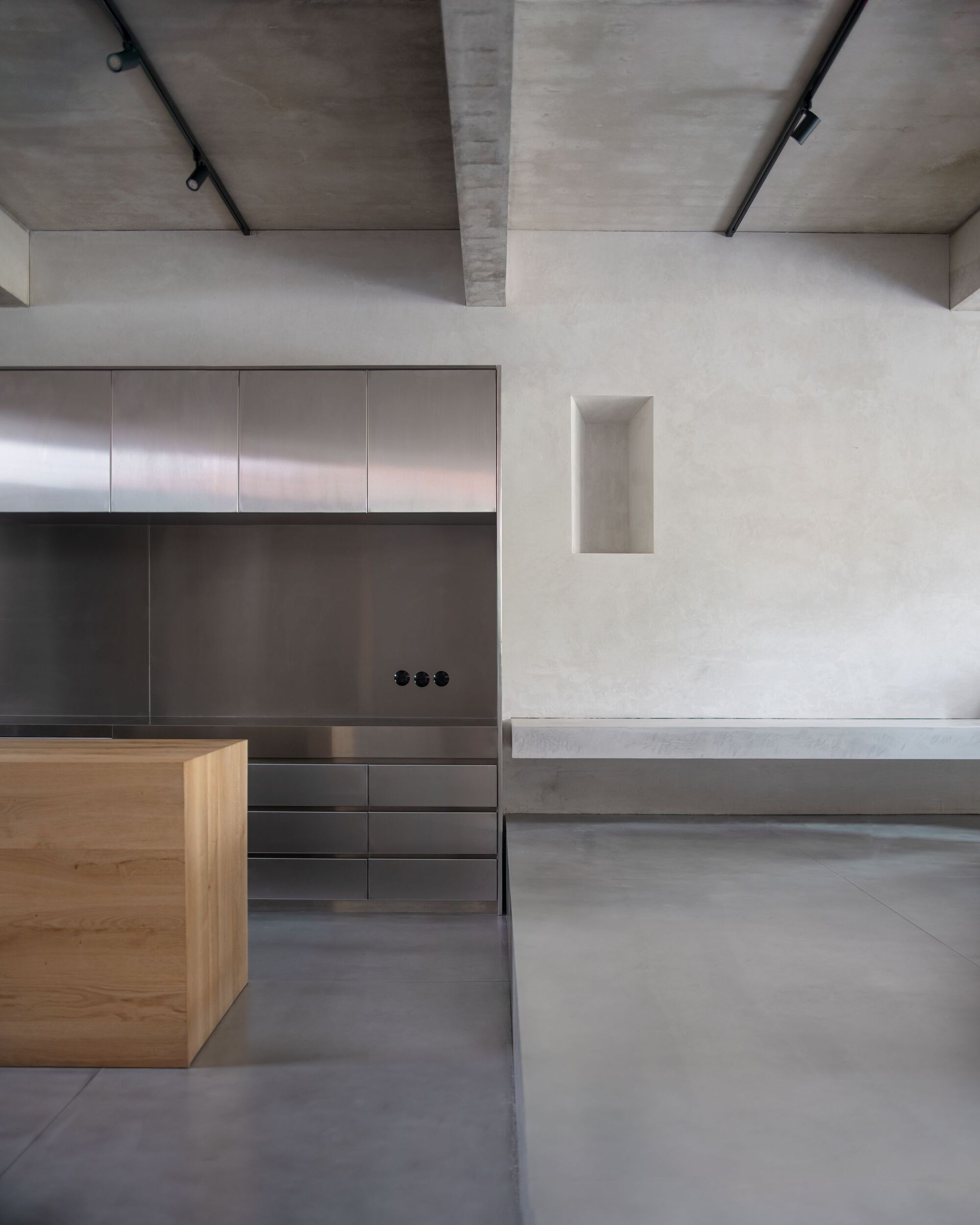 Kitchen with stainless steel cabinets, an oak island and a raised concrete bench beneath a ceiling of exposed beams and track lights