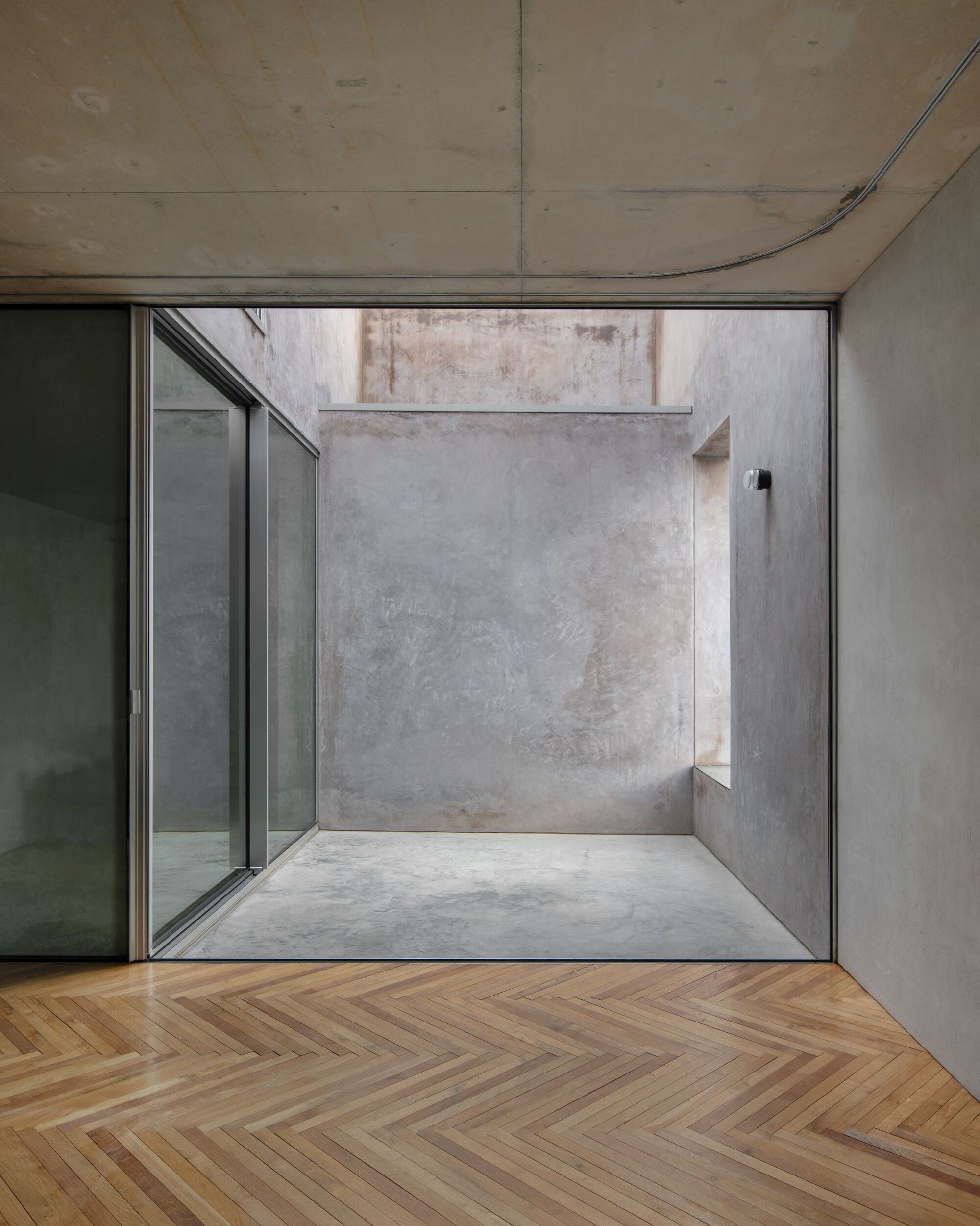 Herringbone timber floor in front of a sliding glass door opening onto a small concrete light well with a recessed niche