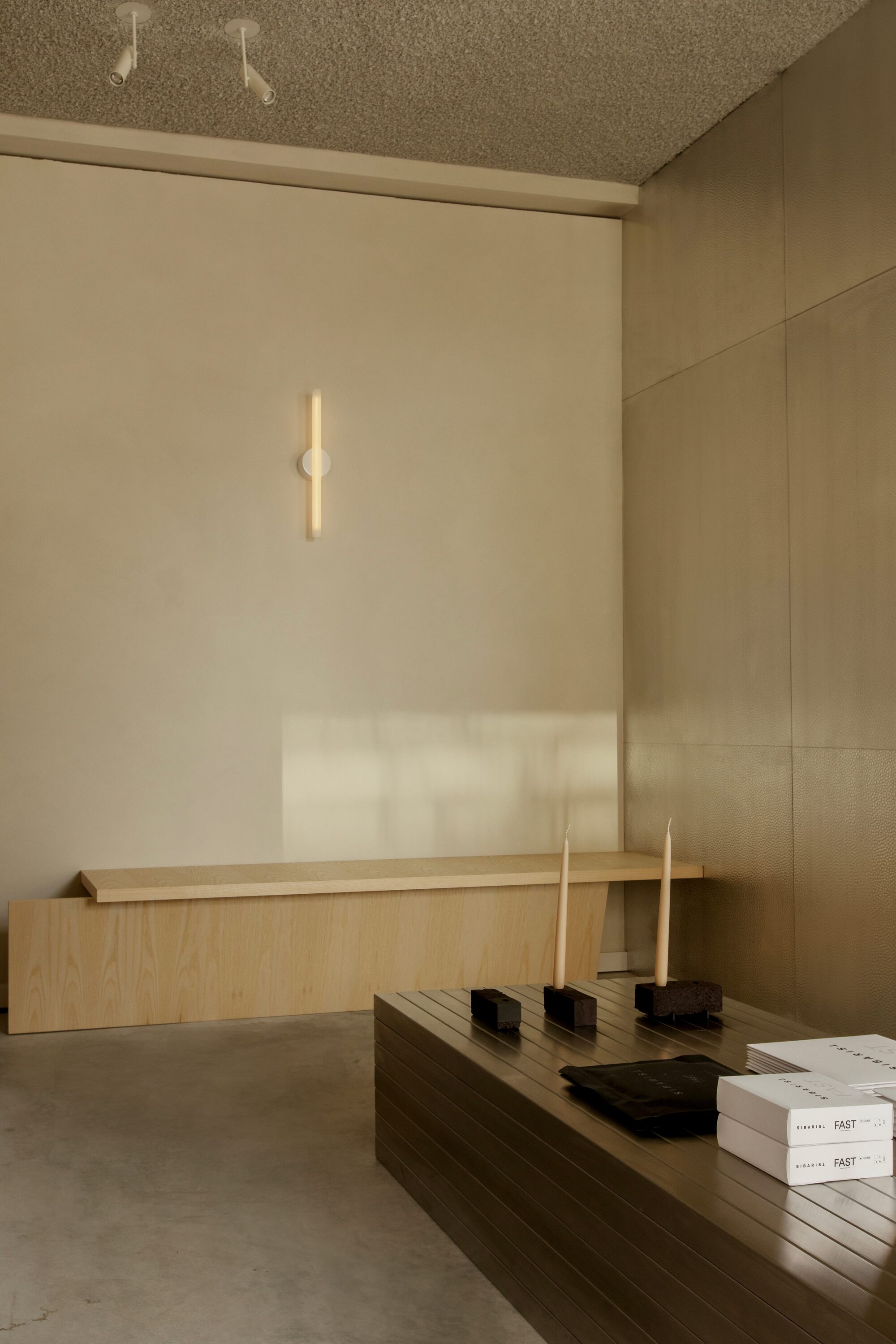 Brass wall light above a oak bench and slatted display table with candles and stacked books in afternoon sun