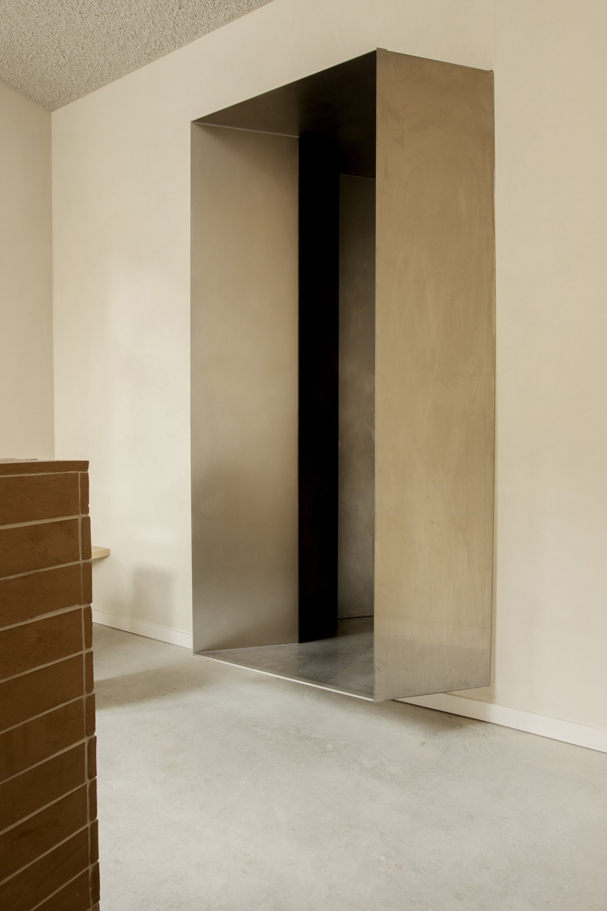 Steel-lined recess set into a plaster wall beside the brick counter edge, over a polished concrete floor