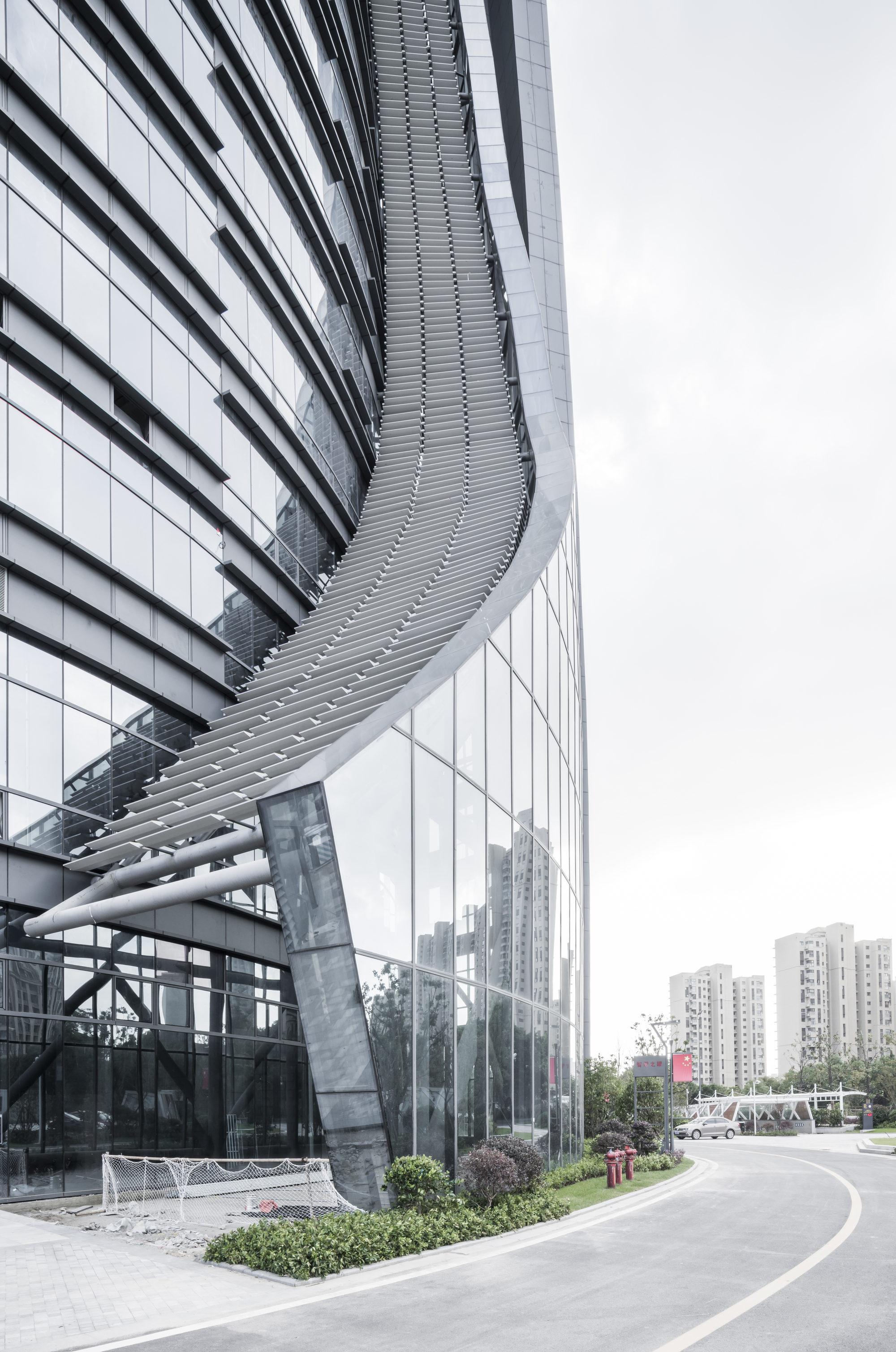 Low corner view of the sweeping louvered ramp curling down the glass facade beside an empty curving road