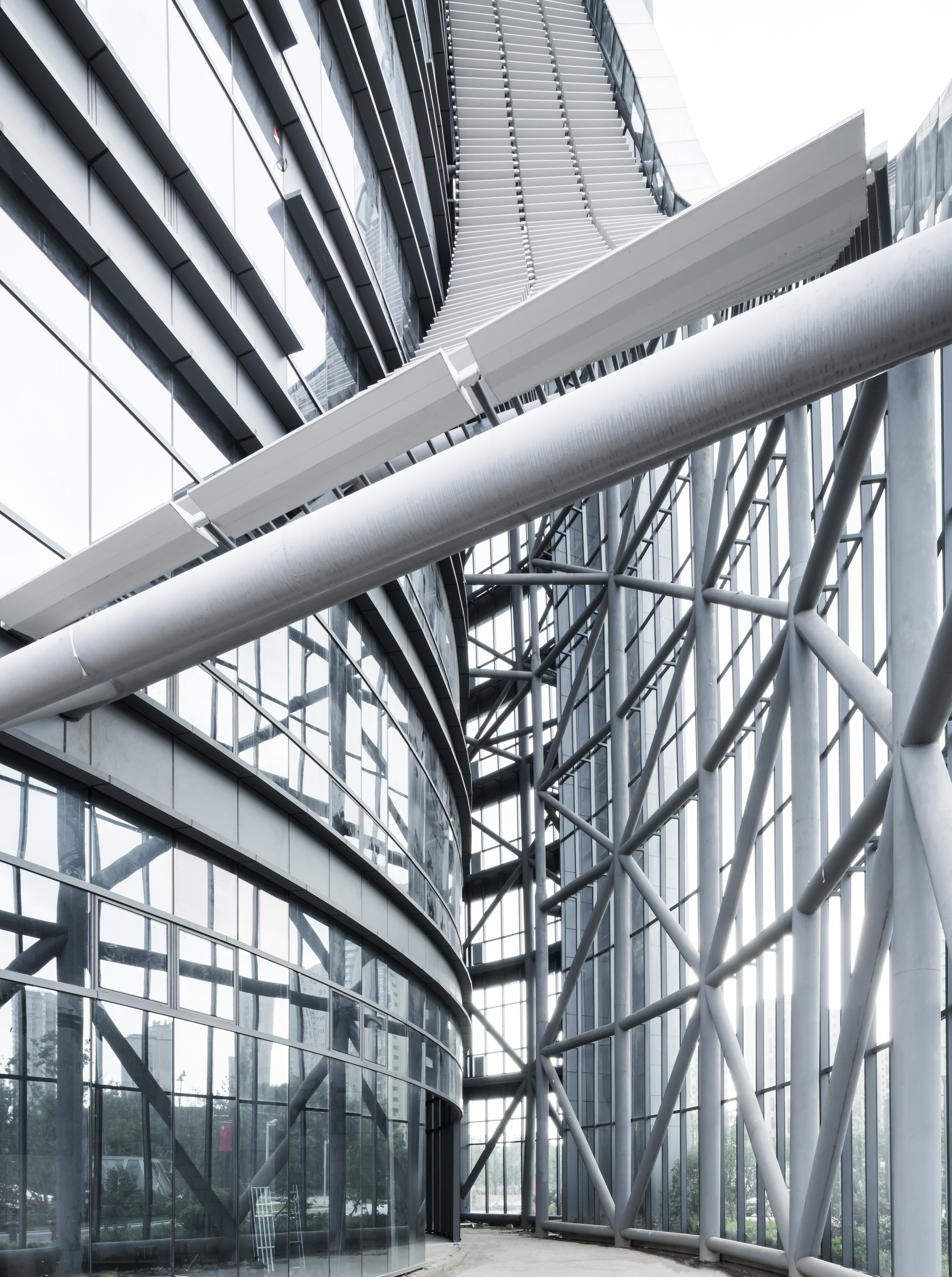 Upward view of white steel tubes, diagonal bracing and louvered canopy at the tower base in soft grey light