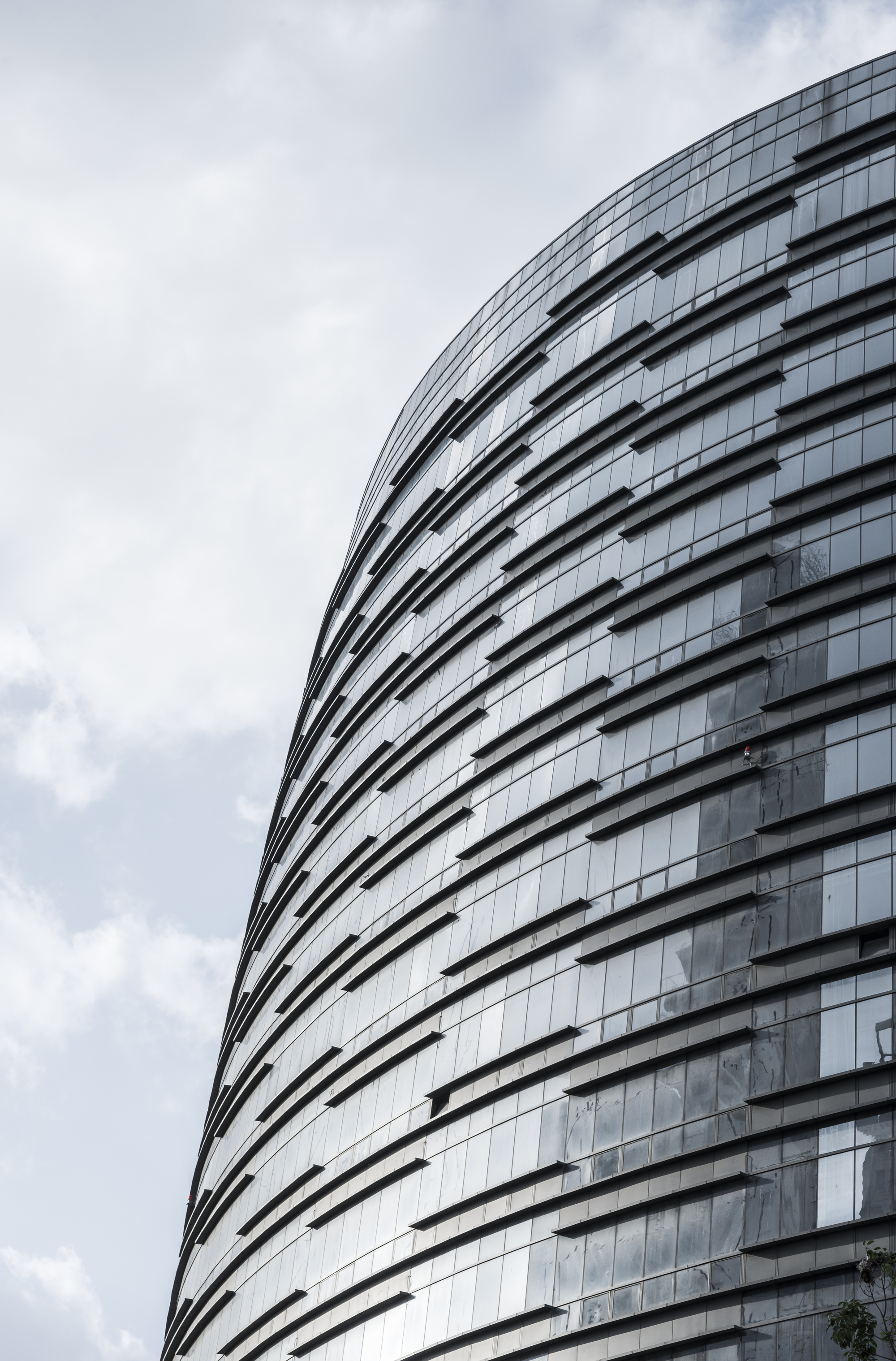 Close-up of the curved glass facade with dark horizontal bands, reflecting clouds against a grey sky