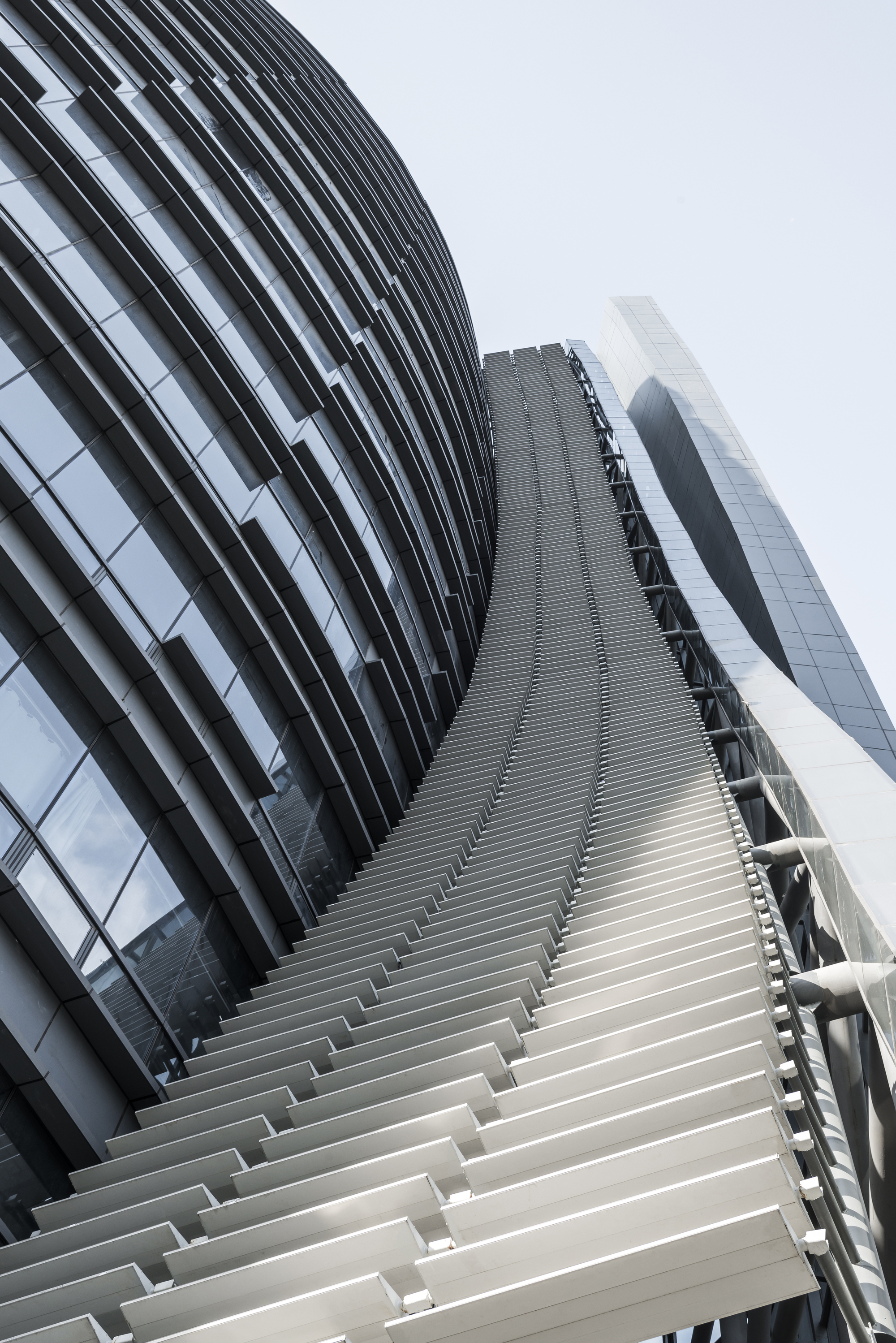 Upward view of white horizontal louvers climbing the curved spine between the glass tower and the neighboring volume