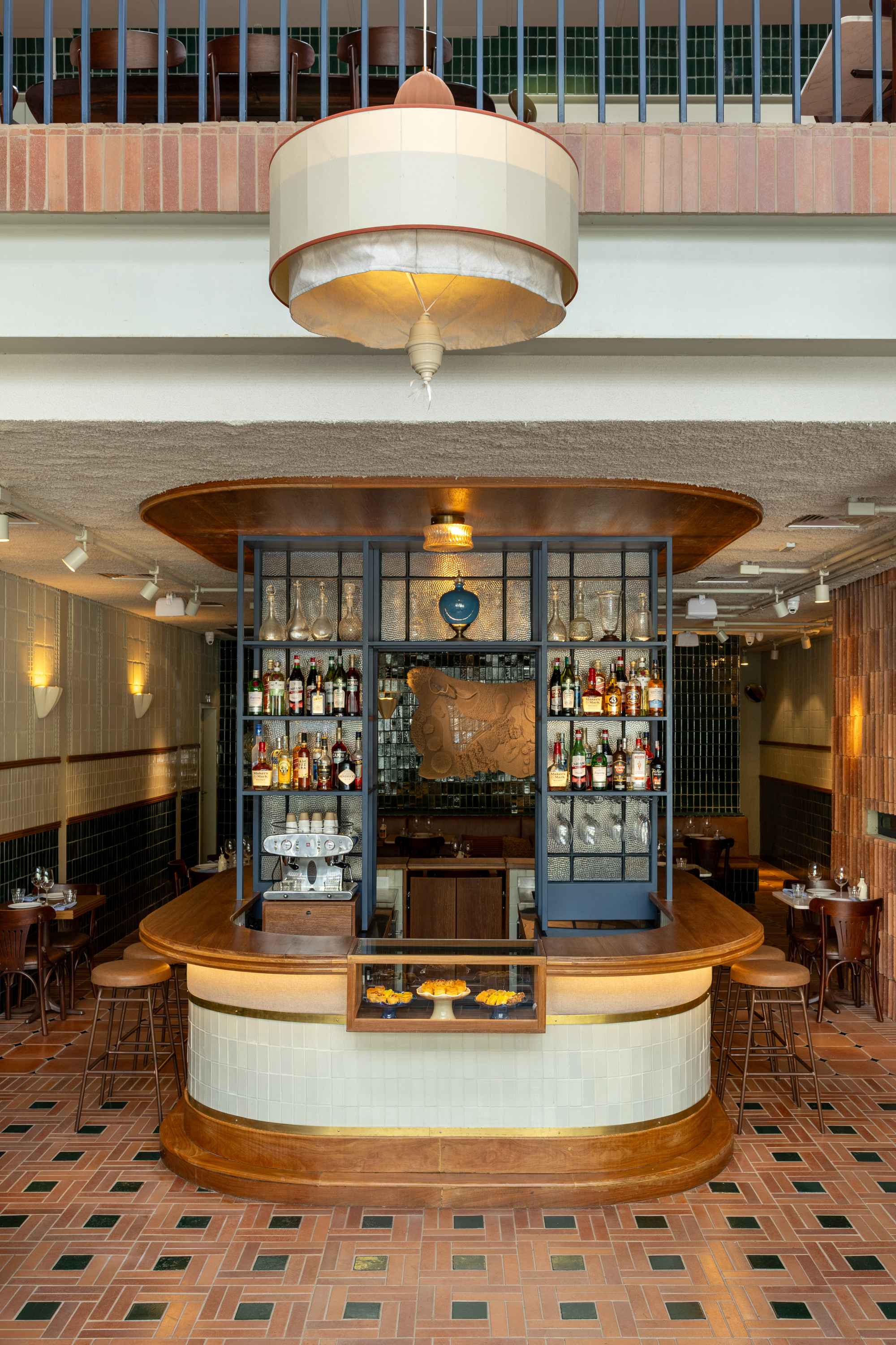 Curved timber and tile bar with a blue-framed bottle shelf and a fabric pendant lamp, lit by warm wall sconces