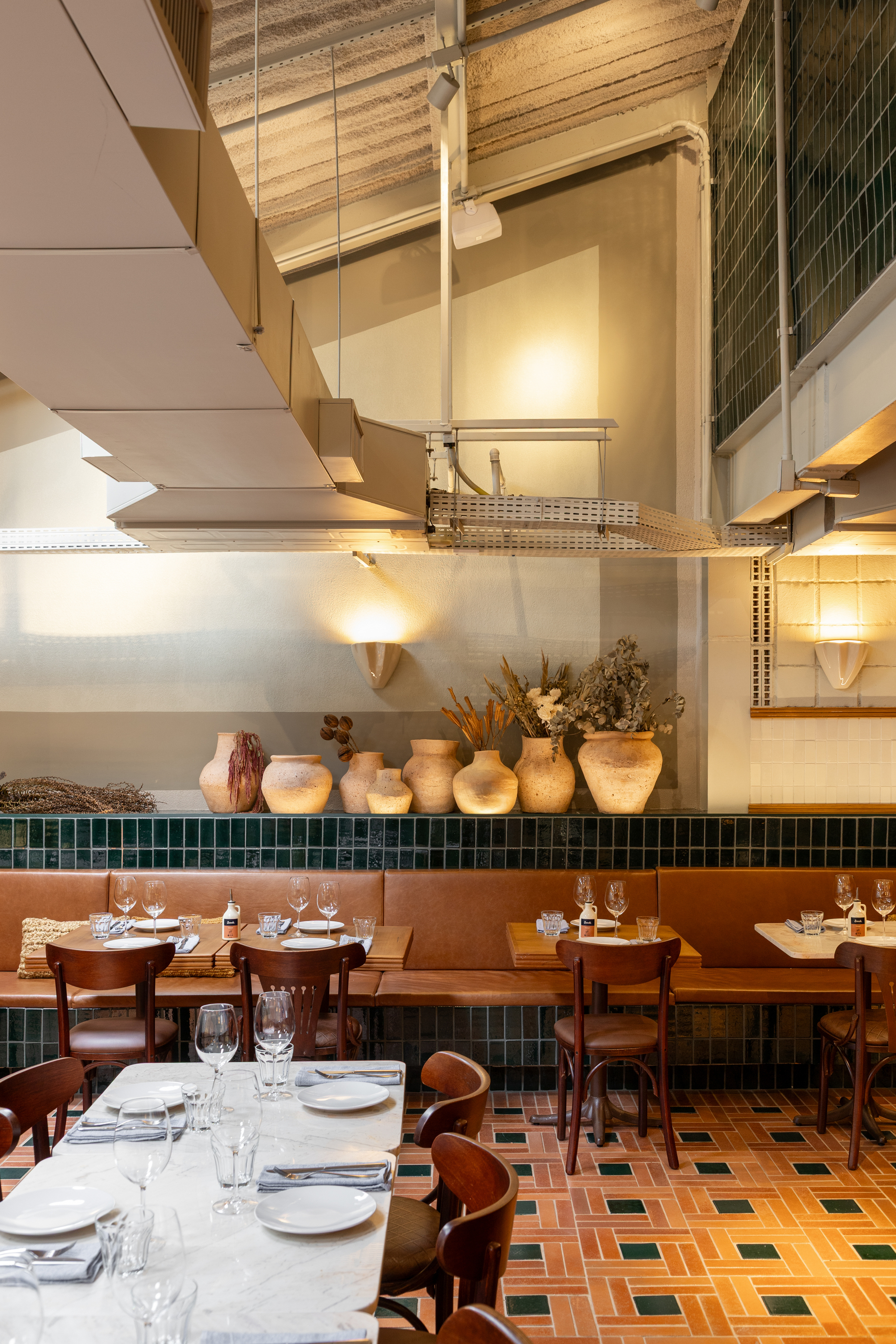 Row of terracotta pots with dried stems on a green tile ledge above banquette seating, with exposed ducts overhead