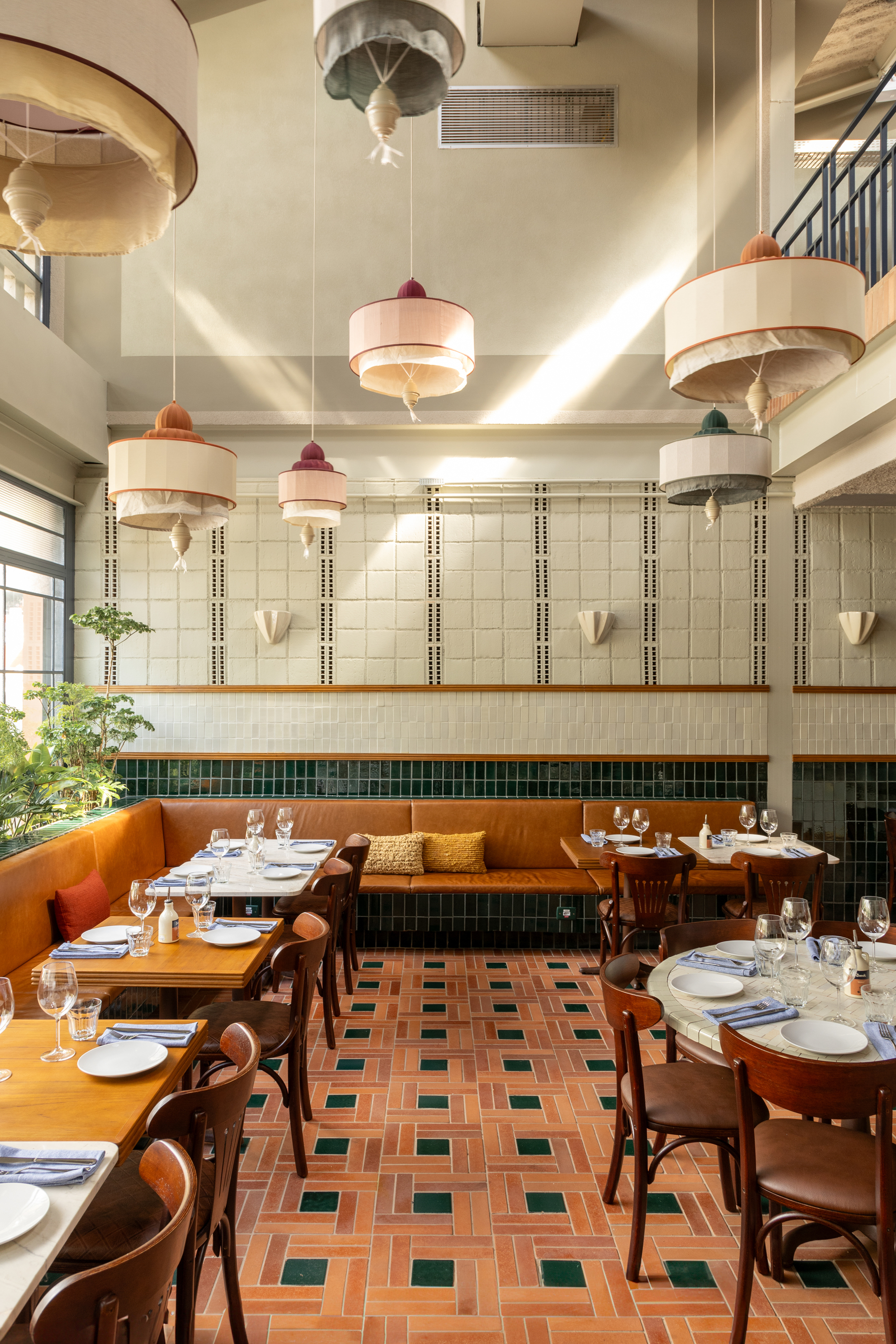 Double-height dining room with pendant lamps, a leather banquette and a patterned terracotta floor lit by diagonal daylight