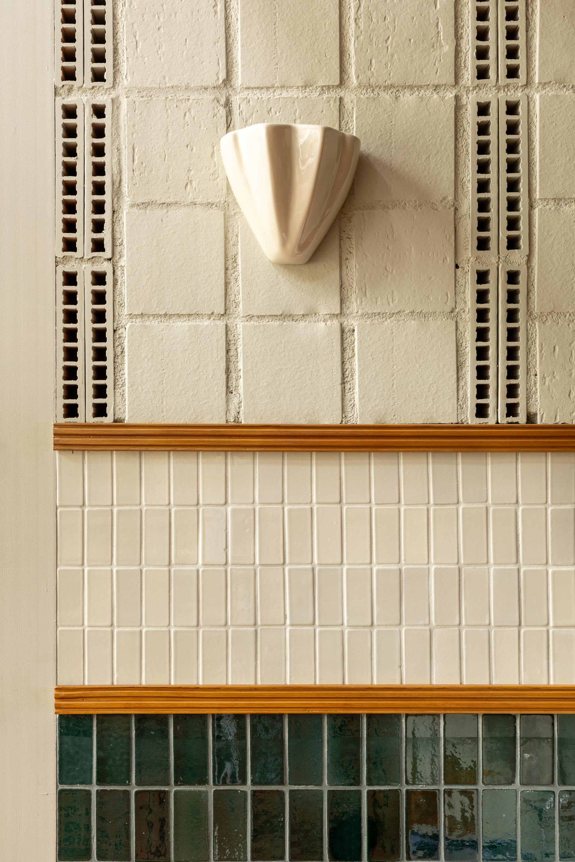 Close-up of a ceramic shell sconce on a perforated cream block wall above bands of cream and green tile