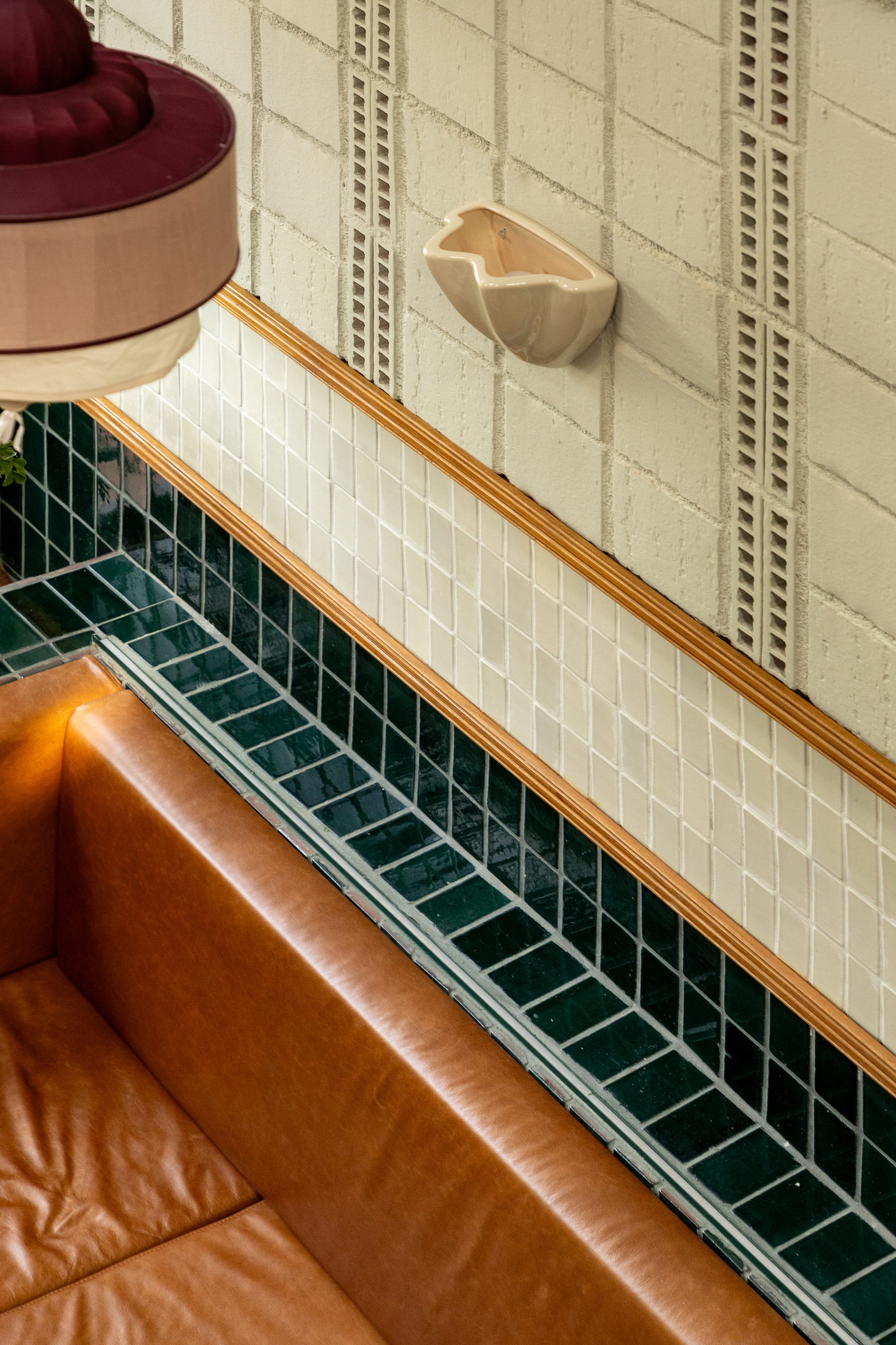 Looking down on a tan leather banquette beside a diagonal run of green tile, timber trim and a maroon pendant shade