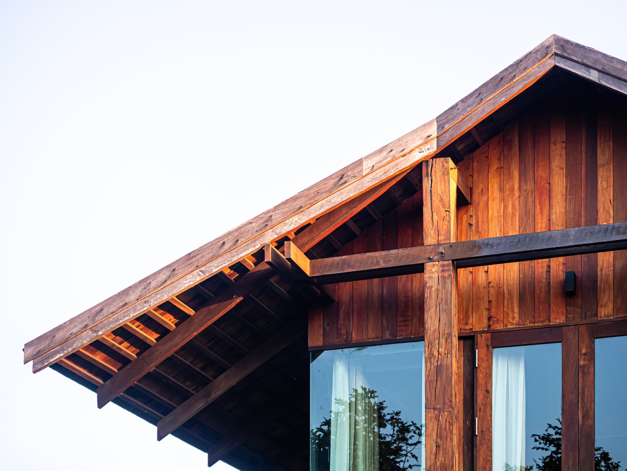 Close-up of the gabled timber roof edge with exposed rafters and a heavy beam, set against a pale hazy sky