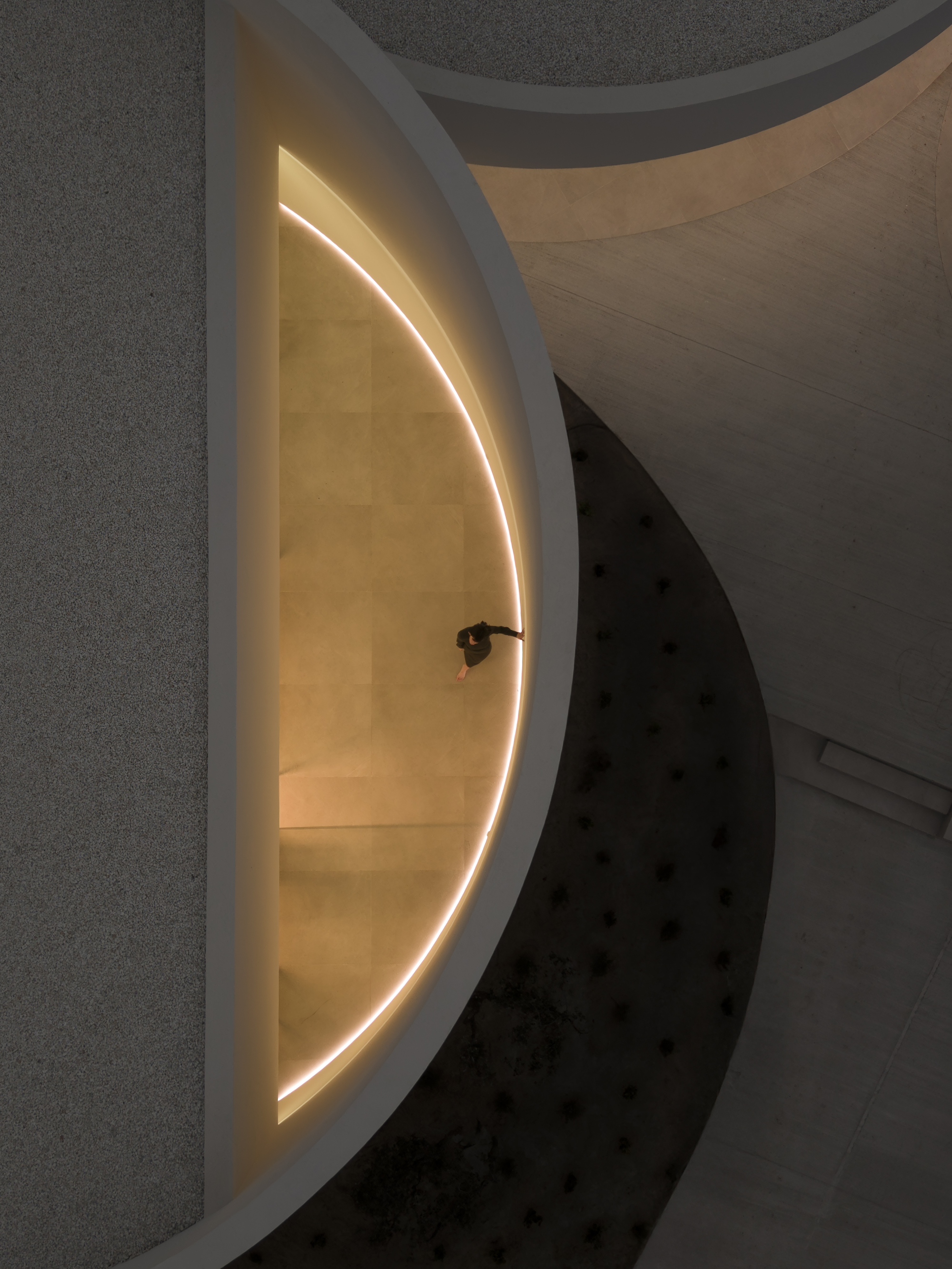Overhead view of a person walking inside a half-moon room edged by a glowing curved light line at night