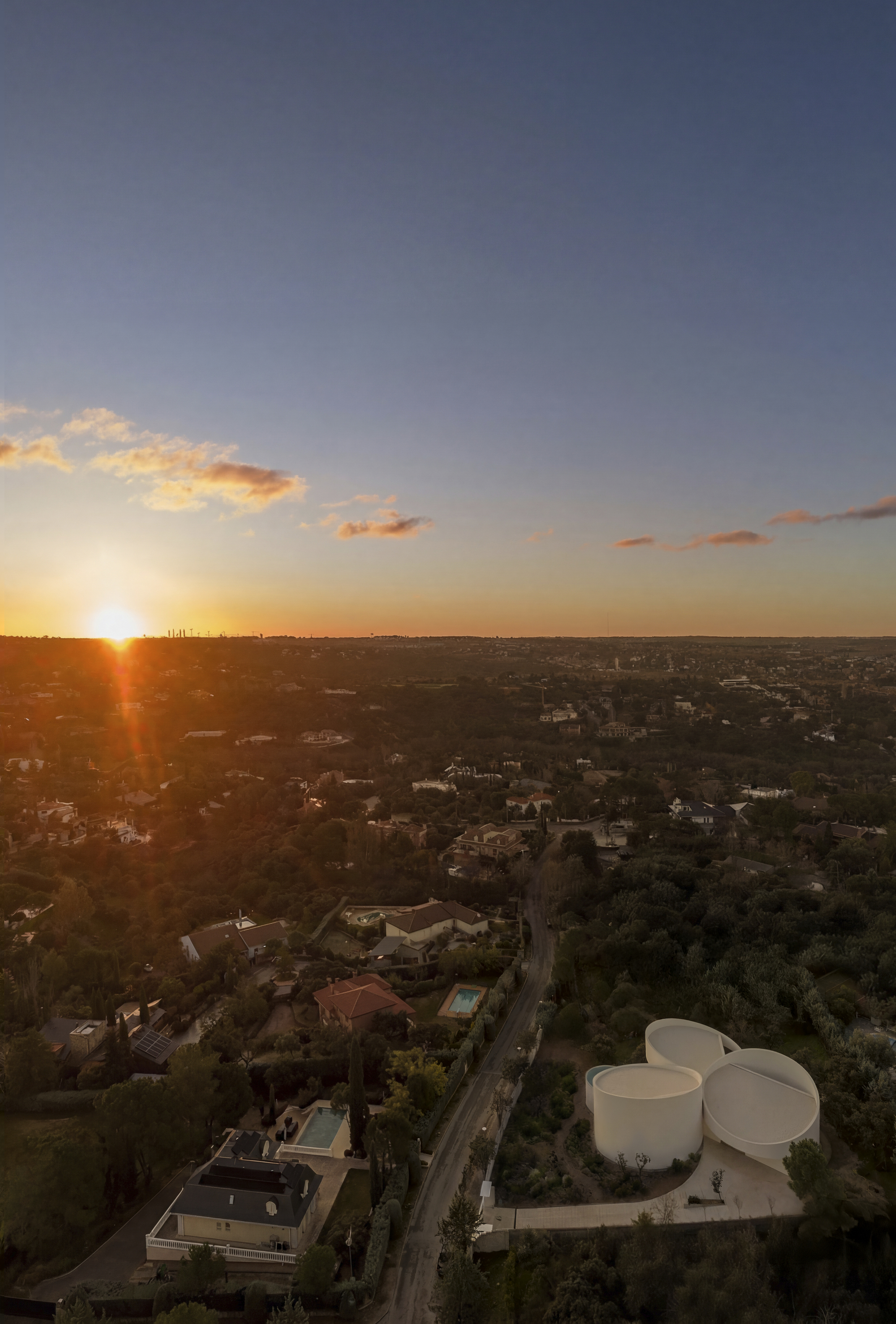 Aerial view of the cluster of round white roofs beside a road, with a suburban neighbourhood stretching toward the setting sun