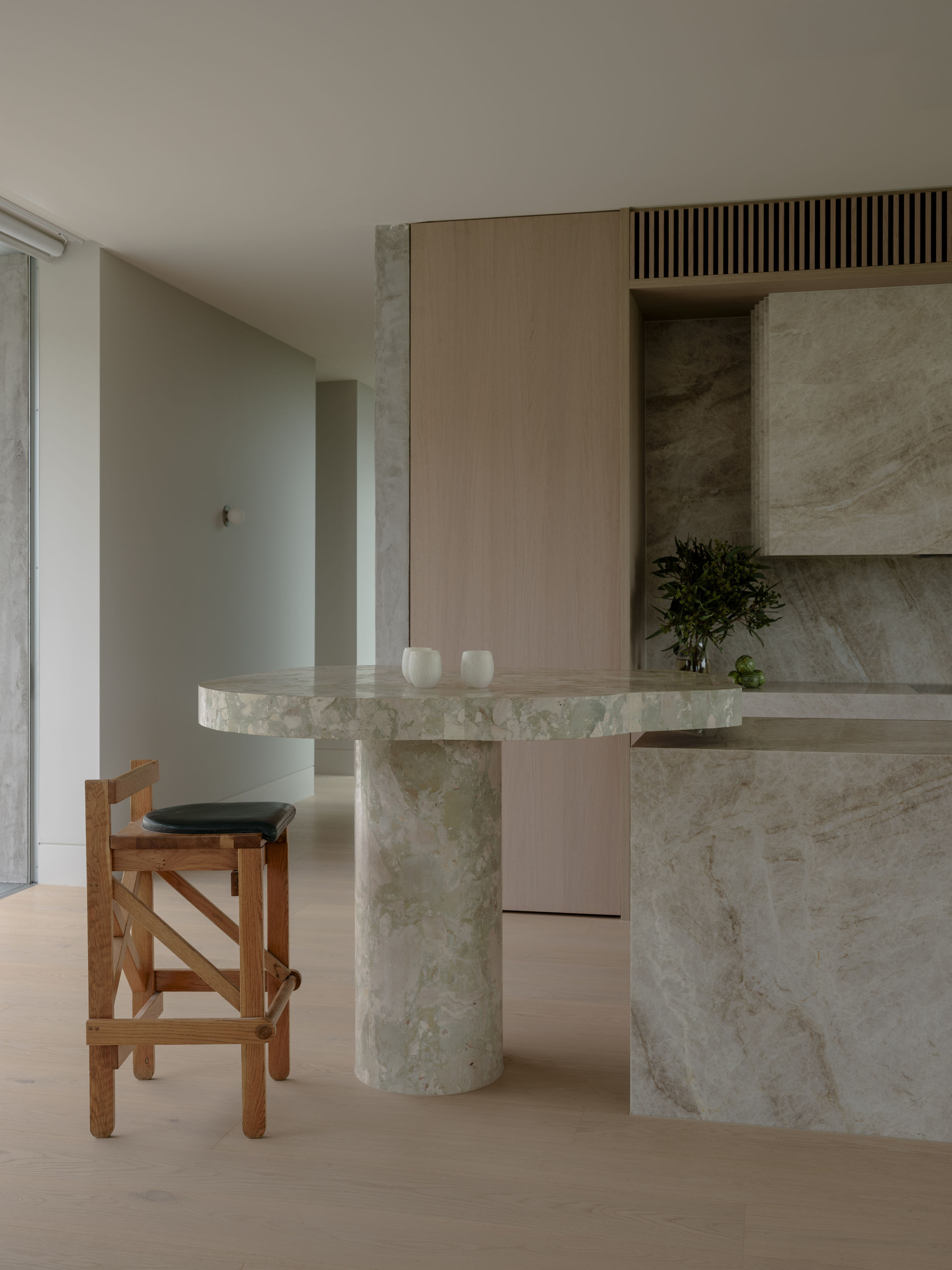Round stone-topped pedestal table beside the kitchen island, with a timber stool in soft daylight