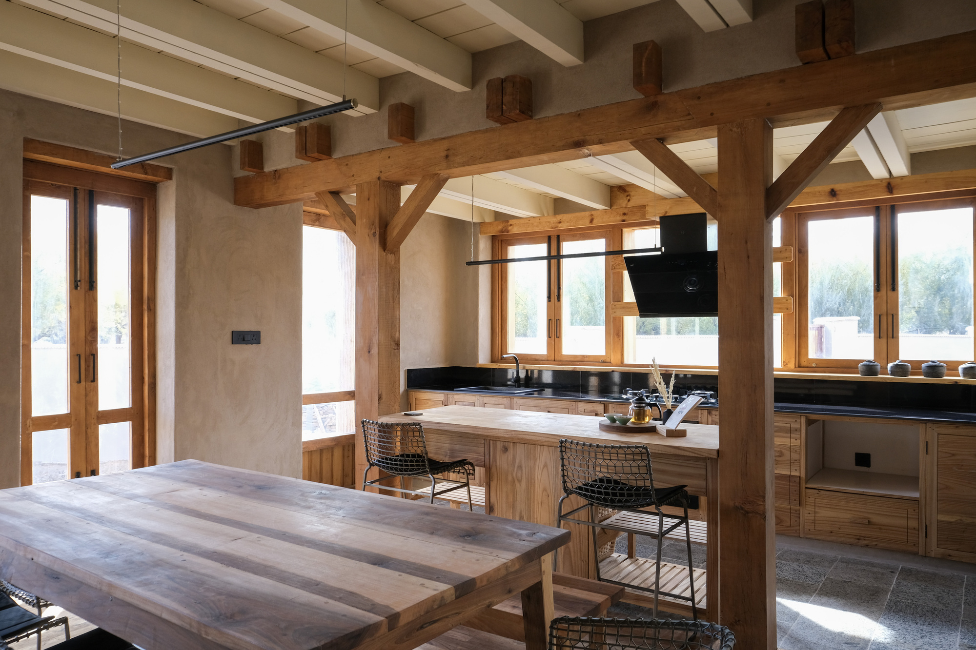 Kitchen with exposed timber posts and beams, a reclaimed wood table and island, and tall windows full of daylight