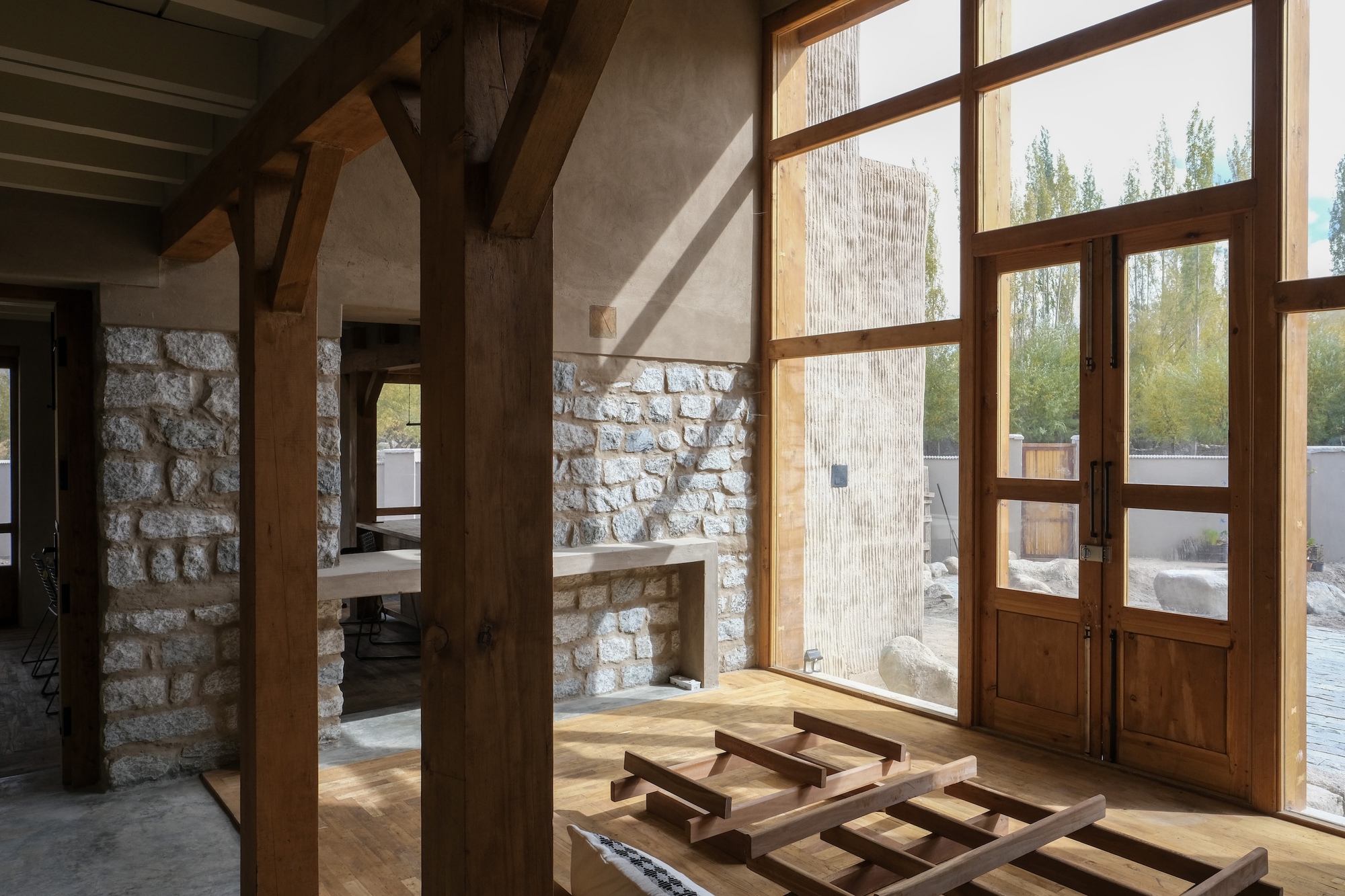 Timber posts and a glazed double door beside a rubble stone wall and plastered counter, lit by low sun
