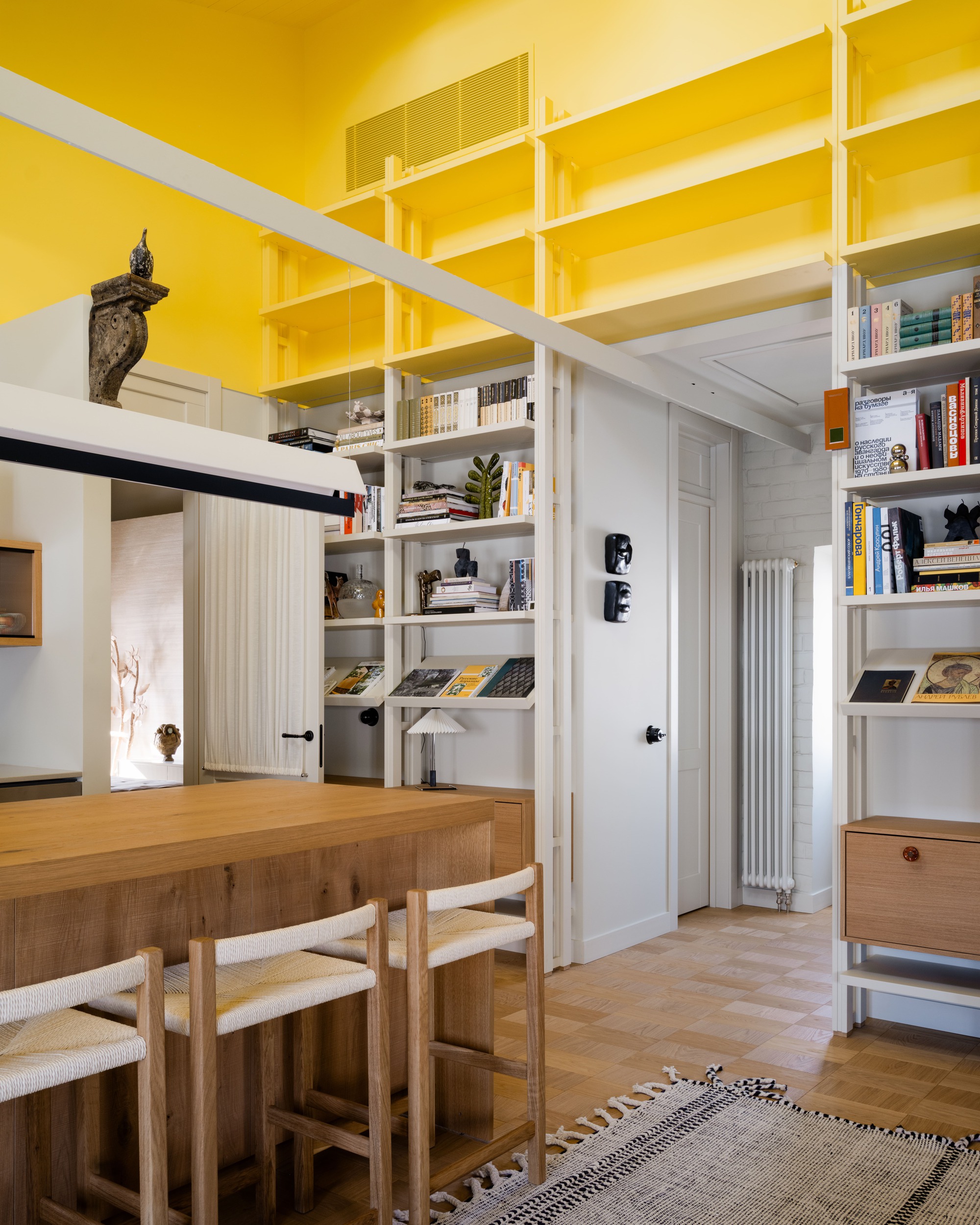 Tall white shelving stacked with books and a ladder beside the oak island, with yellow upper walls and parquet floor