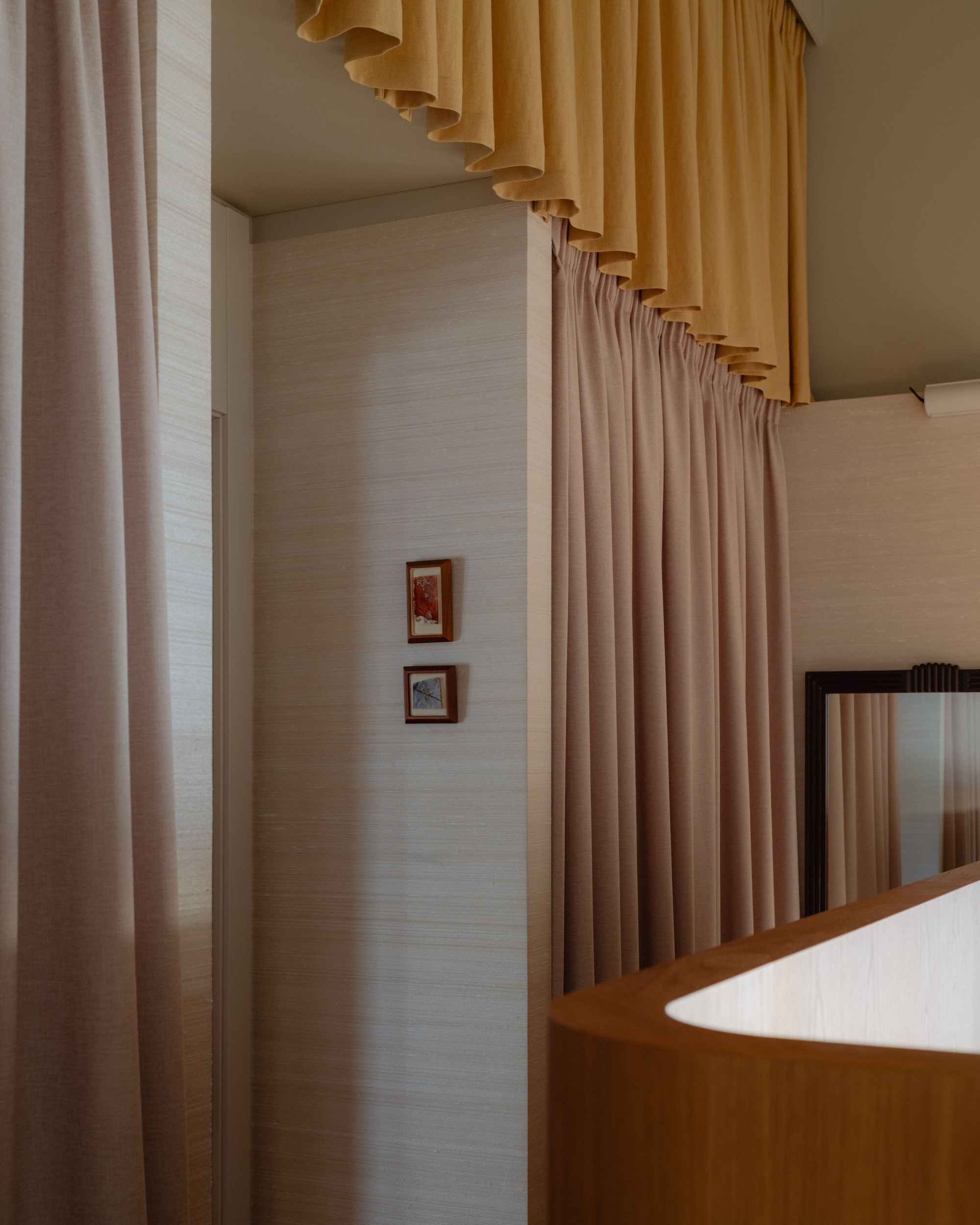Pink linen curtains and a gathered mustard valance beside a grasscloth wall with two small framed pictures and a mirror