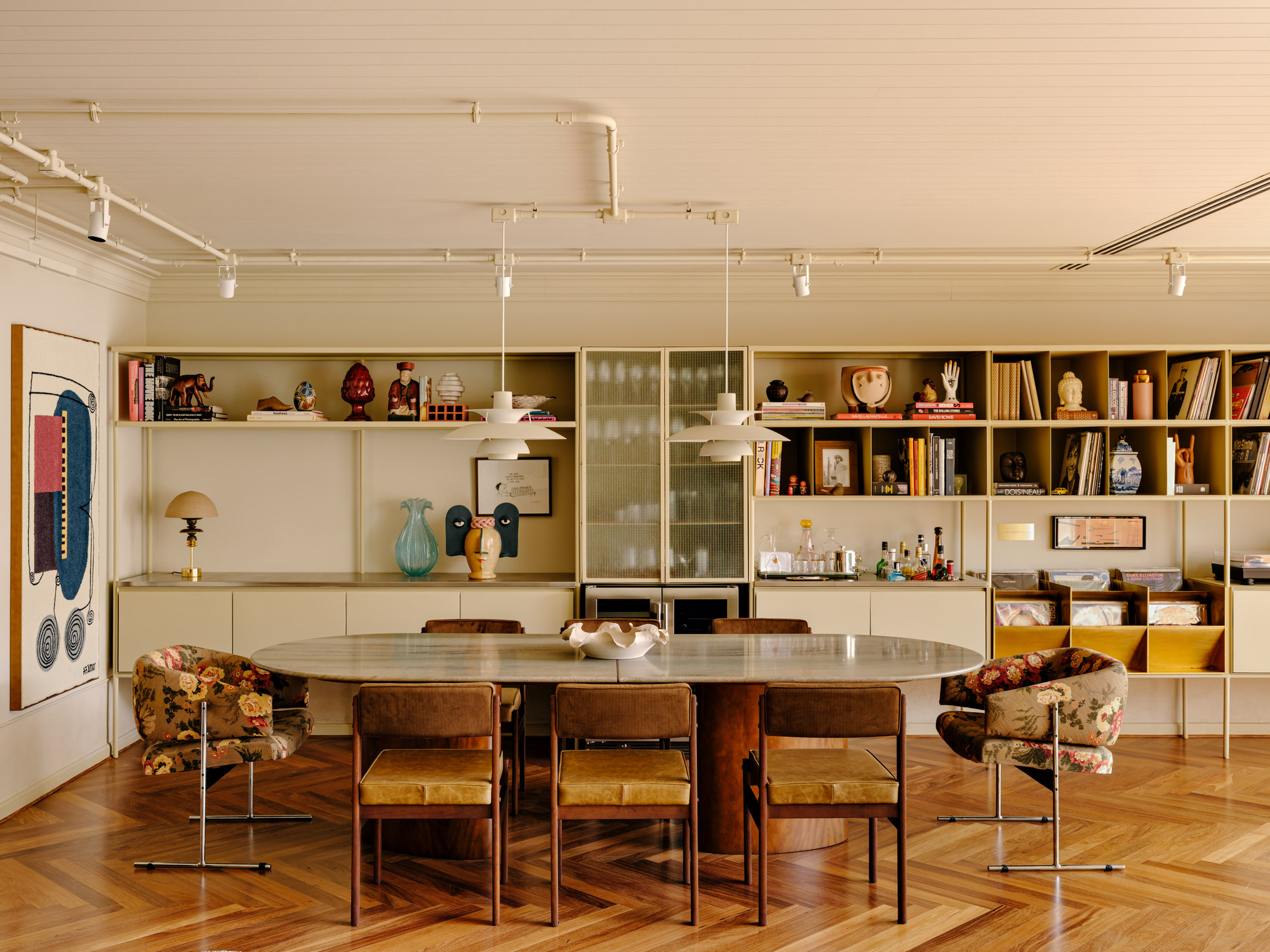 Oval marble dining table in front of cream shelving filled with ceramics and books, with floral armchairs at each end