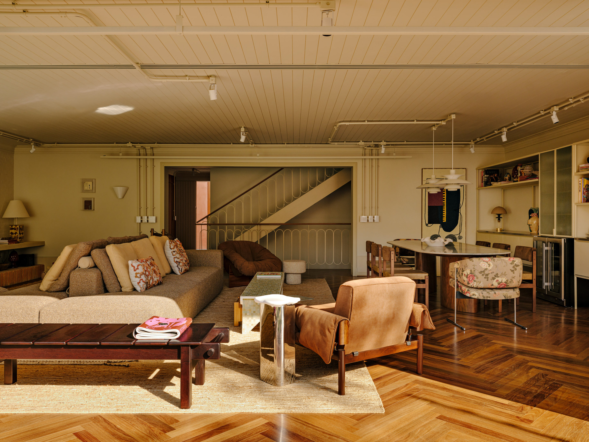 Wide view of the sofa, mirrored side table and tan leather armchair on a jute rug, with the stair behind in low sun