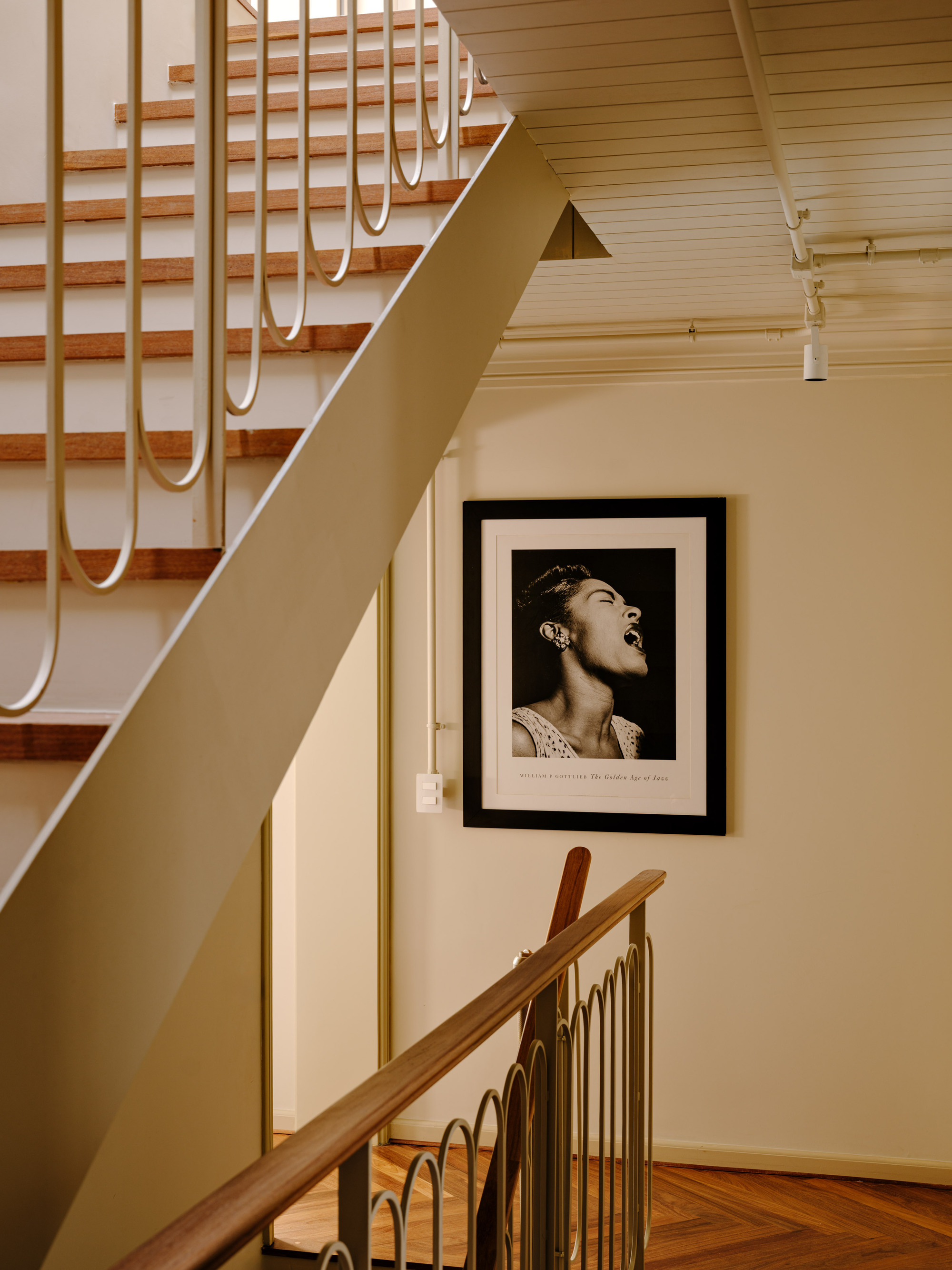 Underside of the stair and a framed black-and-white portrait on a cream wall above a looped balustrade and parquet landing