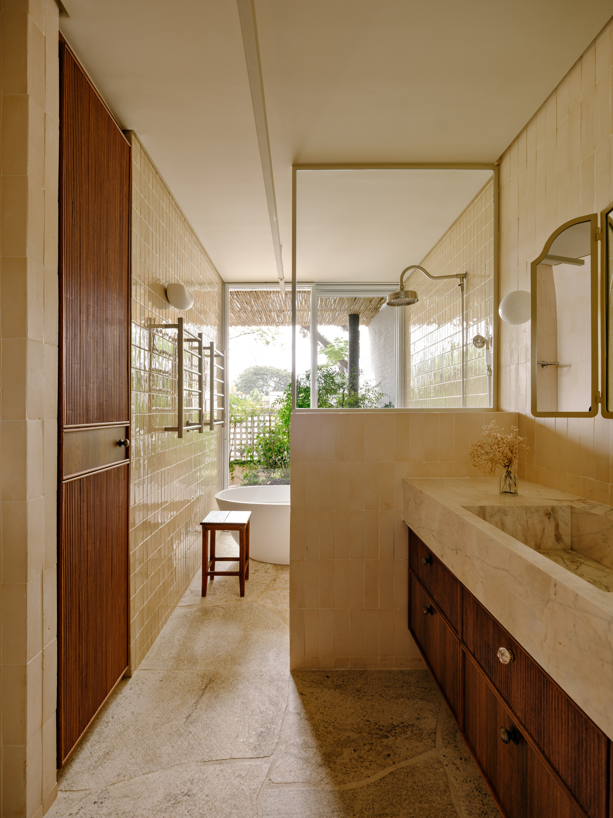 Bathroom with cream glazed tile walls, a marble basin on a timber vanity and a freestanding tub facing a garden