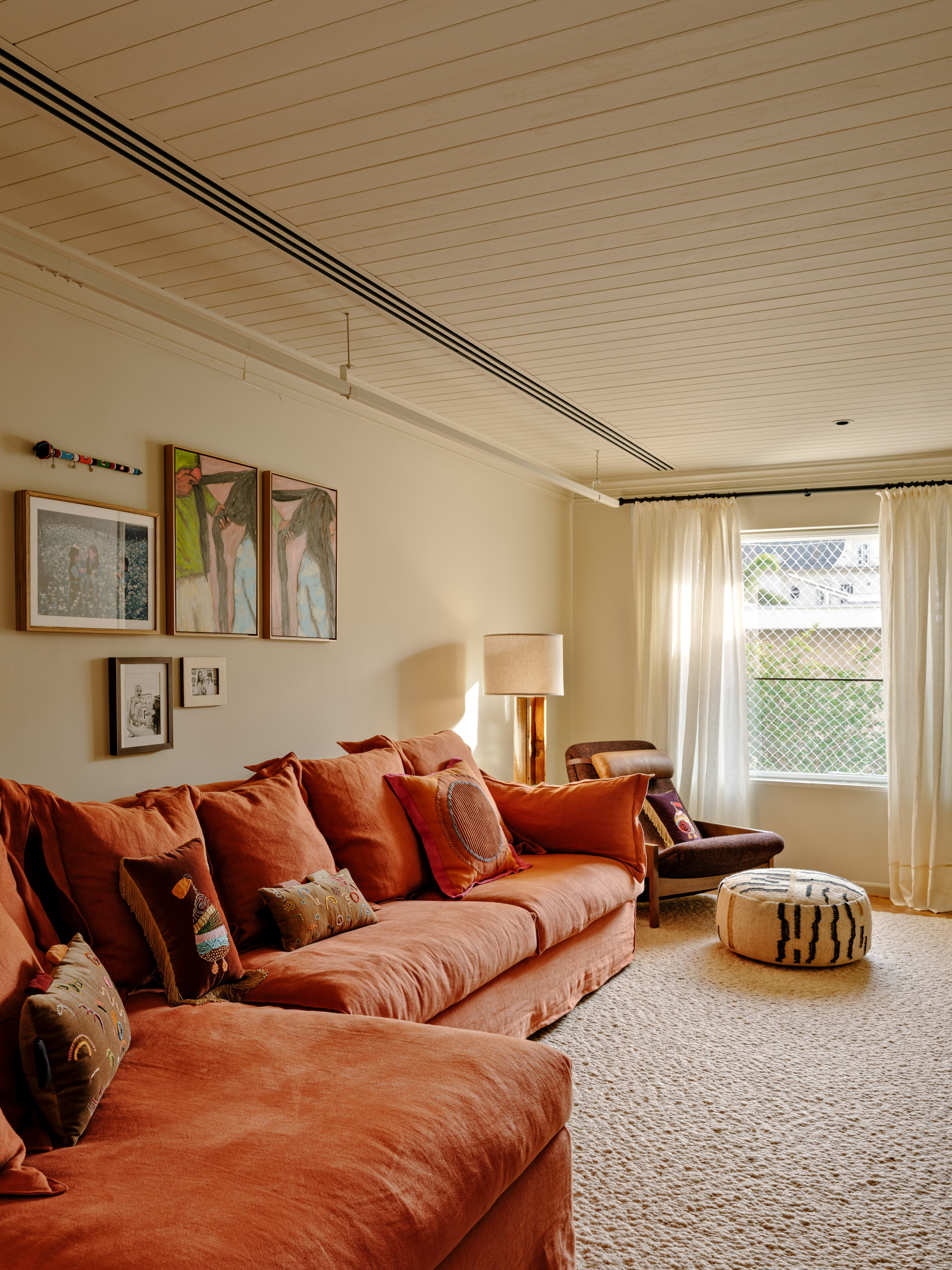 Rust linen sectional sofa with patterned cushions beneath a gallery of framed art, with afternoon light through sheer curtains